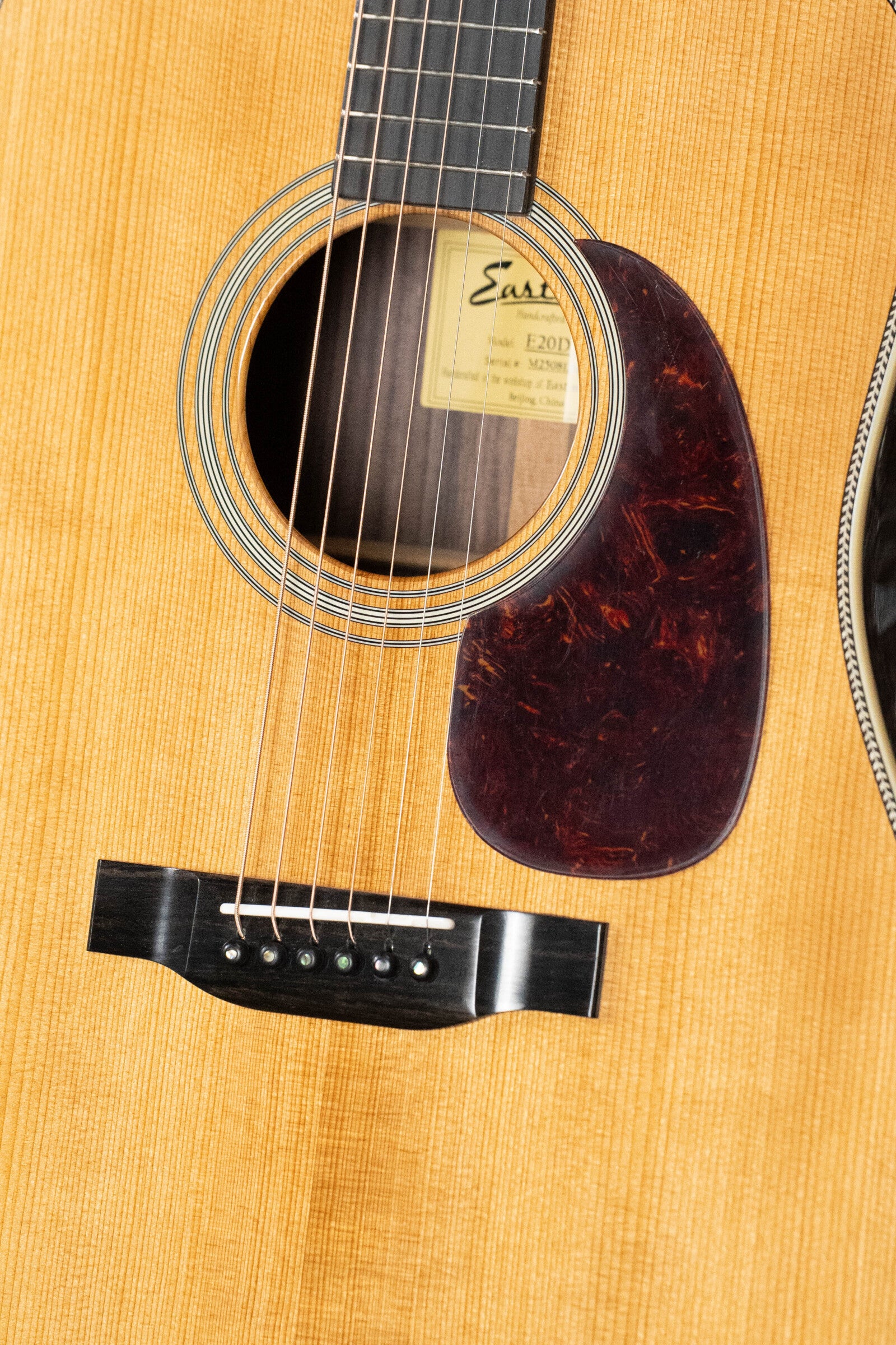 Close-up of the Eastman Guitars E20D-TC Thermo-Cured Adirondack/Rosewood Dreadnought Acoustic Guitar #8128, highlighting its sound hole, strings, dark pickguard, label, natural wood finish, and Adirondack Spruce top.