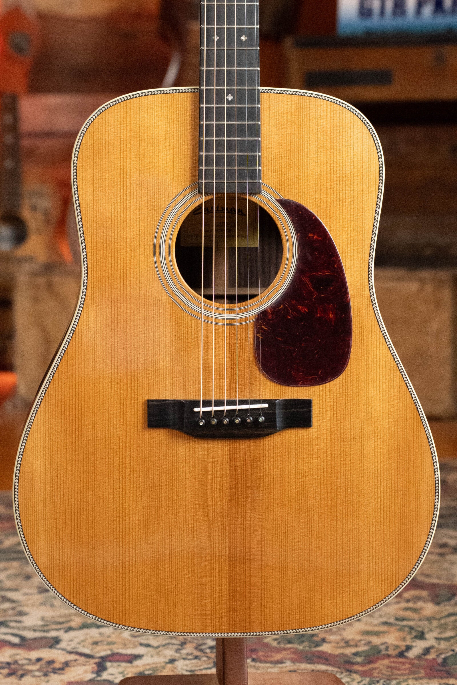 A close-up of the Eastman Guitars E20D-TC Thermo-Cured Adirondack/Rosewood Dreadnought Acoustic Guitar #8128 with natural wood finish, Adirondack spruce top, dark pickguard, and six strings against a rustic wood and rug backdrop.