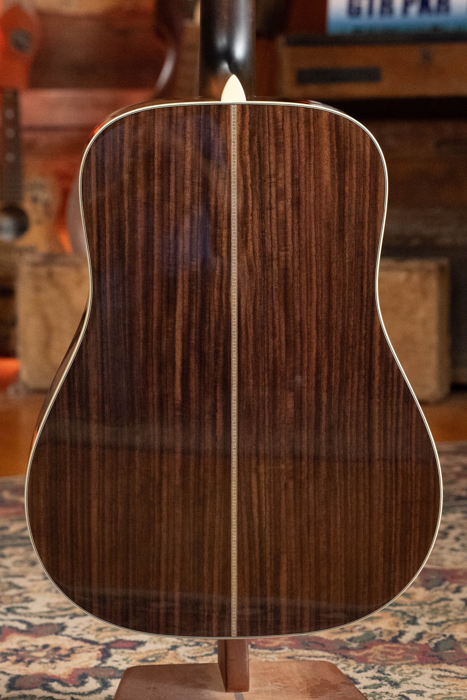 The back of the Eastman Guitars E20D-TC Thermo-Cured Adirondack/Rosewood Dreadnought Acoustic Guitar #8128 features a glossy dark rosewood finish with a contrasting center inlay, displayed on a patterned rug in a cozy wooden room.