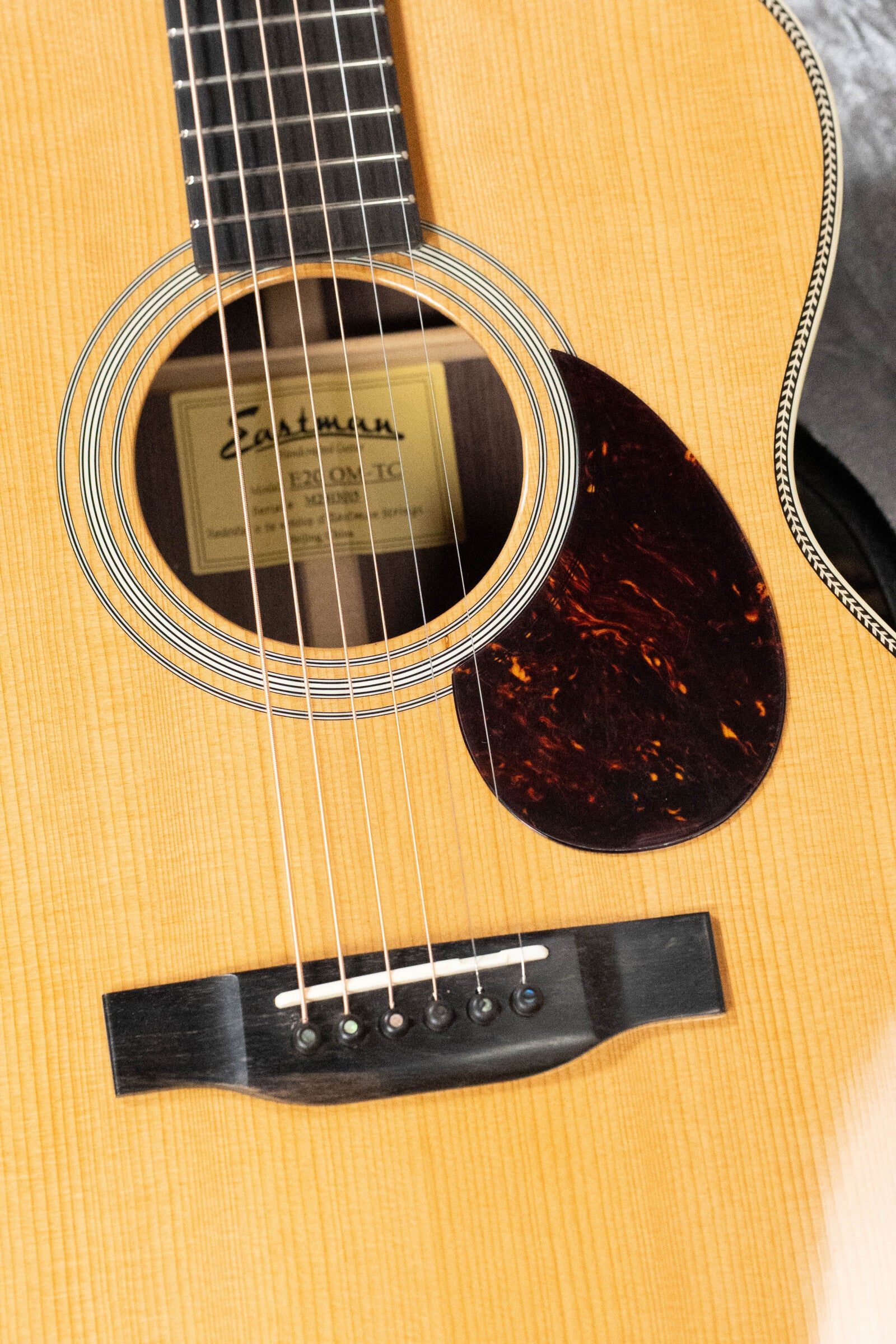 Close-up of an Eastman Guitars E20OM-TC Thermo-Cured Adirondack/Rosewood Orchestra Model Acoustic Guitar #3015 body, featuring rosewood soundboard, black pickguard, strings, fretboard section, and label inside the soundhole.