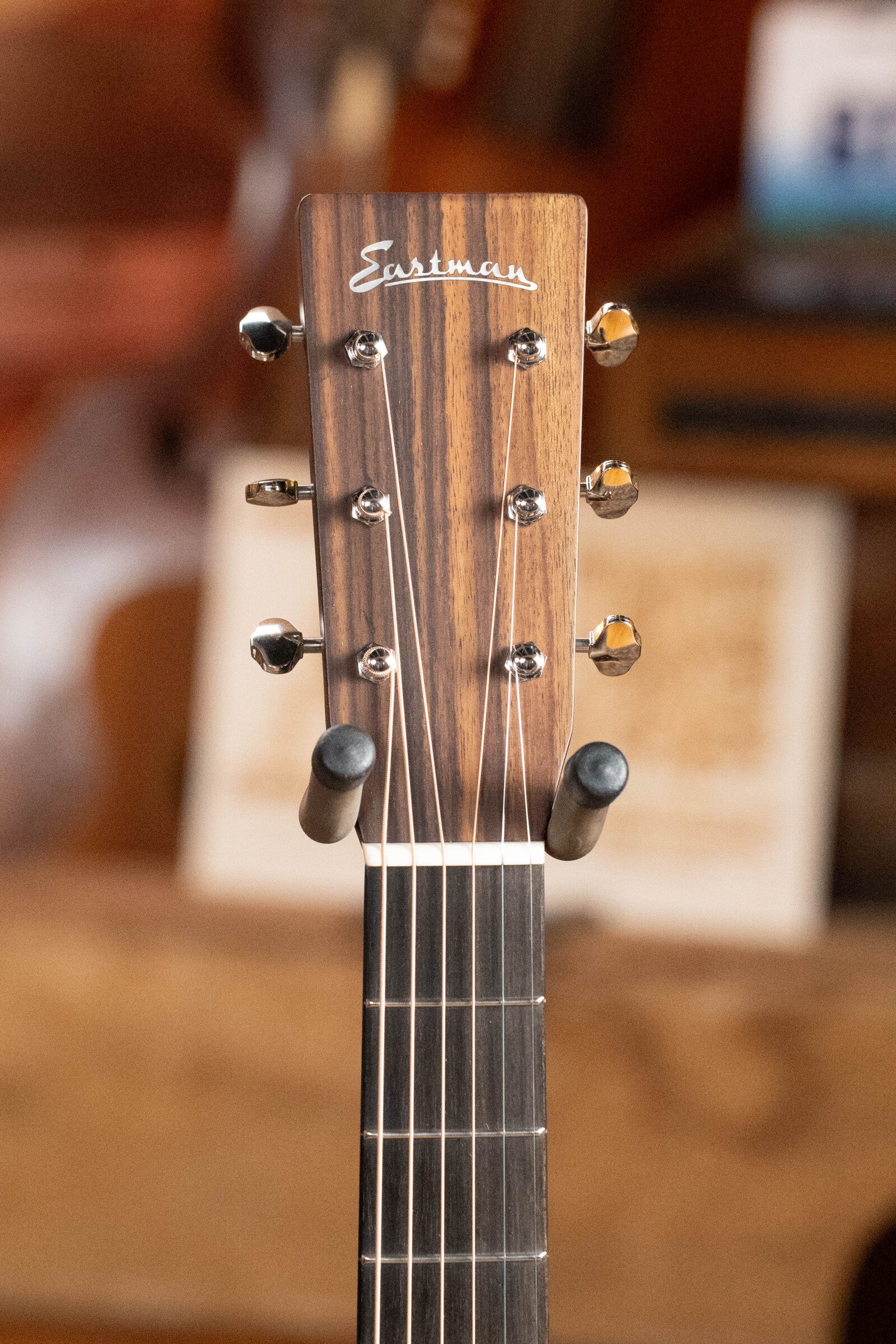 Close-up of the headstock of an Eastman Guitars E20OM-TC Thermo-Cured Adirondack/Rosewood Orchestra Model Acoustic Guitar #3015, showing six tuning pegs, the Eastman logo, and part of the neck against a wooden background.