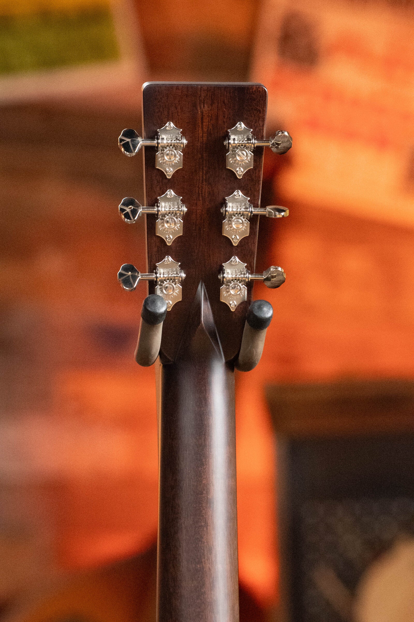 Close-up of the back of an Eastman Guitars E20OM-TC Thermo-Cured Adirondack/Rosewood Orchestra Model Acoustic Guitar #3015 headstock with six silver tuners, wooden neck, and a warm blurred background; the guitar rests on a stand.