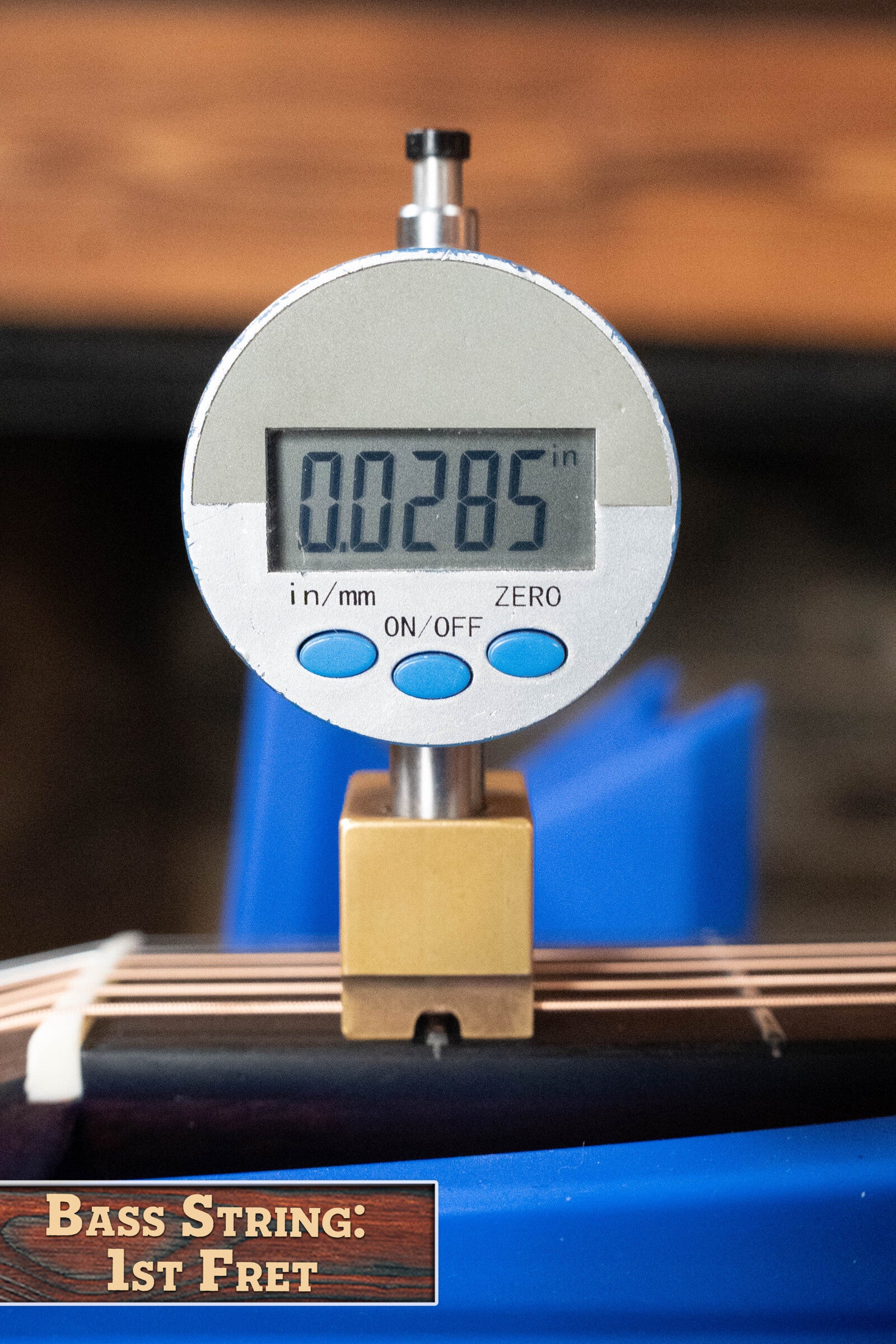 A digital caliper measures a bass string at the 1st fret, displaying 0.0285 inches. A label reads “Bass String: 1st Fret.” Blue and wood tones evoke the Eastman Guitars E20OM-TC Thermo-Cured Adirondack/Rosewood #3015.