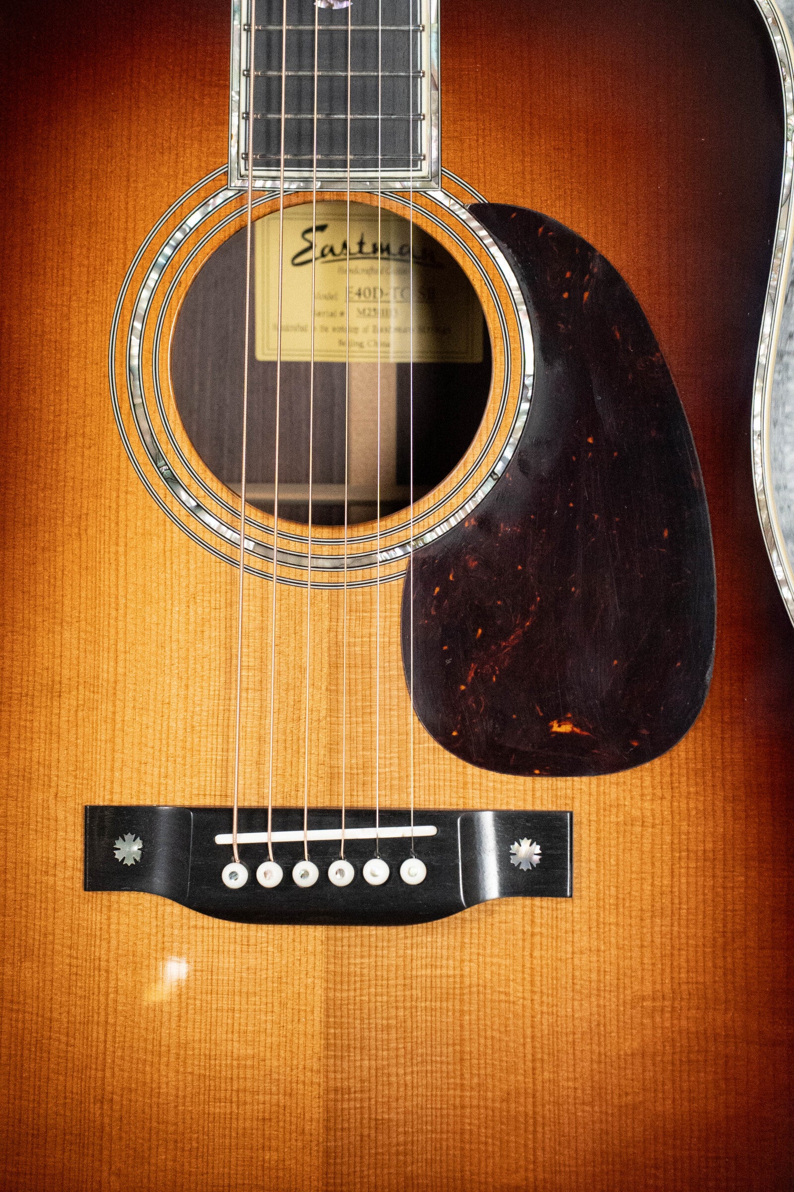 Close-up of an Eastman Guitars E40D-TC-SB Sunburst Dreadnought Acoustic Guitar #1113, showcasing its Thermo-cured AAA Adirondack top, rich rosewood back/sides, soundhole, strings, bridge, pickguard, and inside label.