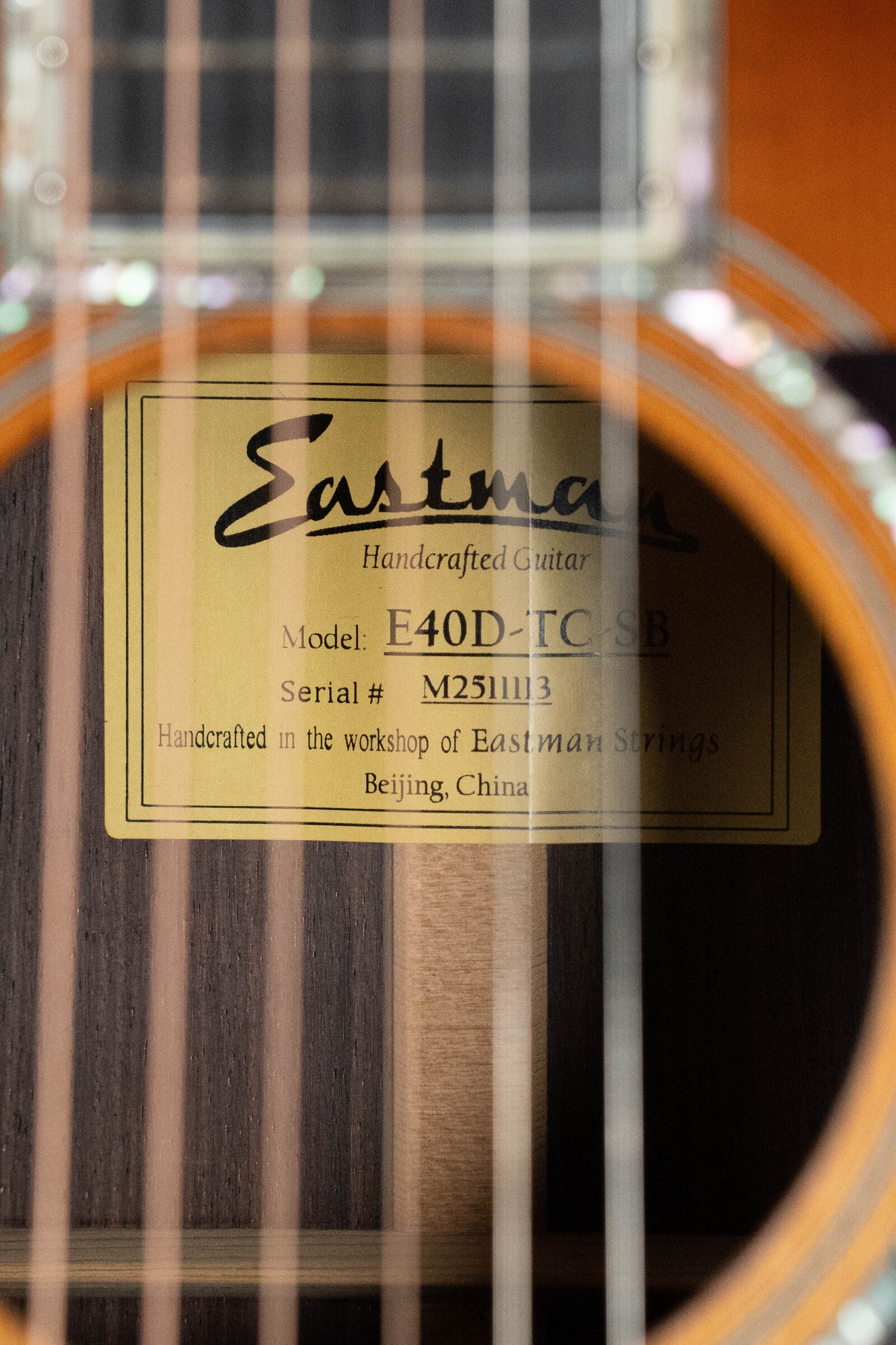 Close-up of an Eastman Guitars E40D-TC-SB Sunburst Dreadnought (#1113) sound hole, showing the inside label. Features thermo-cured AAA Adirondack spruce top and rosewood back/sides, with strings visible in the foreground.