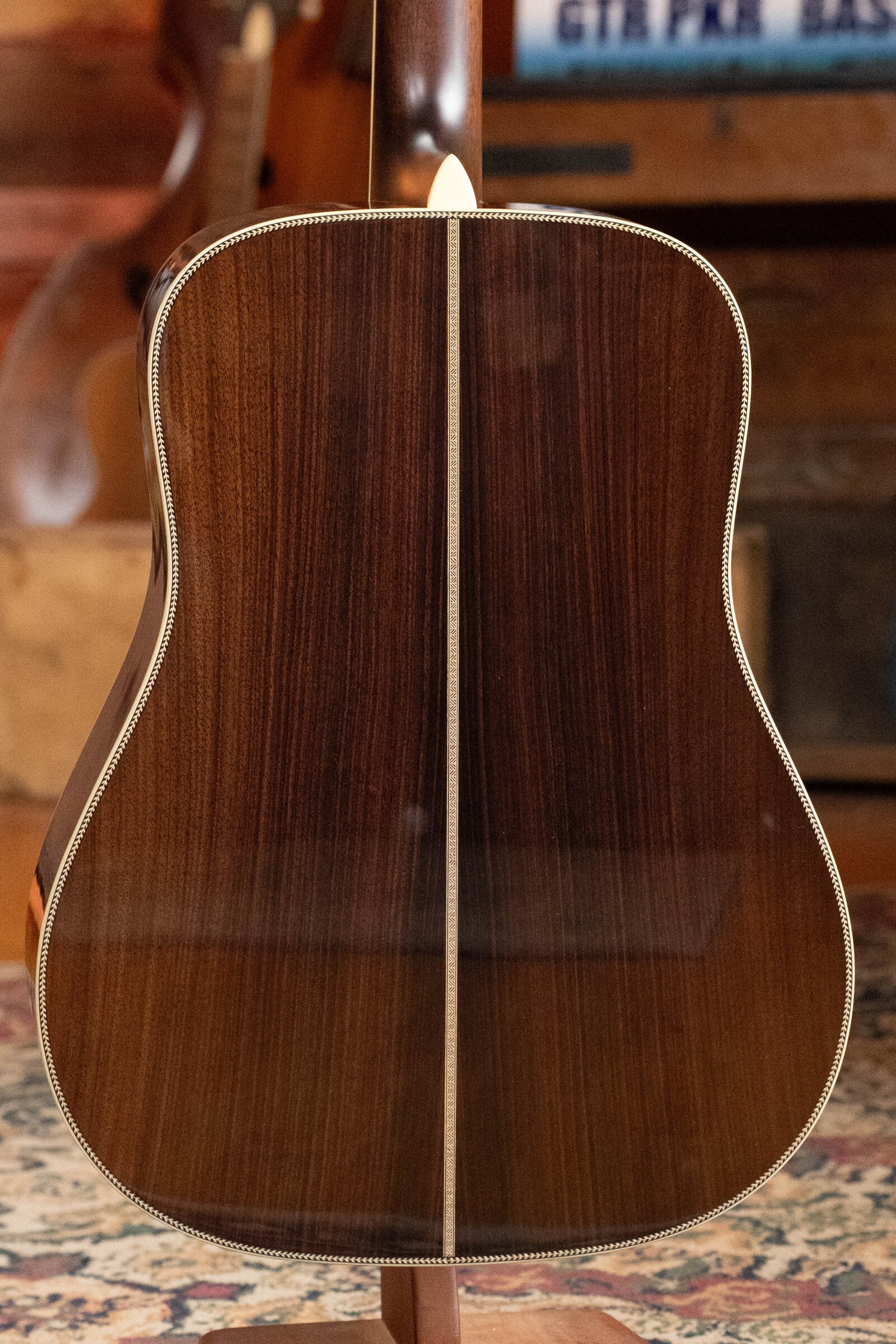 The image shows the back of an Eastman Guitars E40D-TC-SB Thermo-cured AAA Grade Adirondack/Rosewood Sunburst Dreadnought Acoustic Guitar #1113, featuring a rich rosewood finish, center seam, and detailed binding, standing upright on a patterned rug indoors.