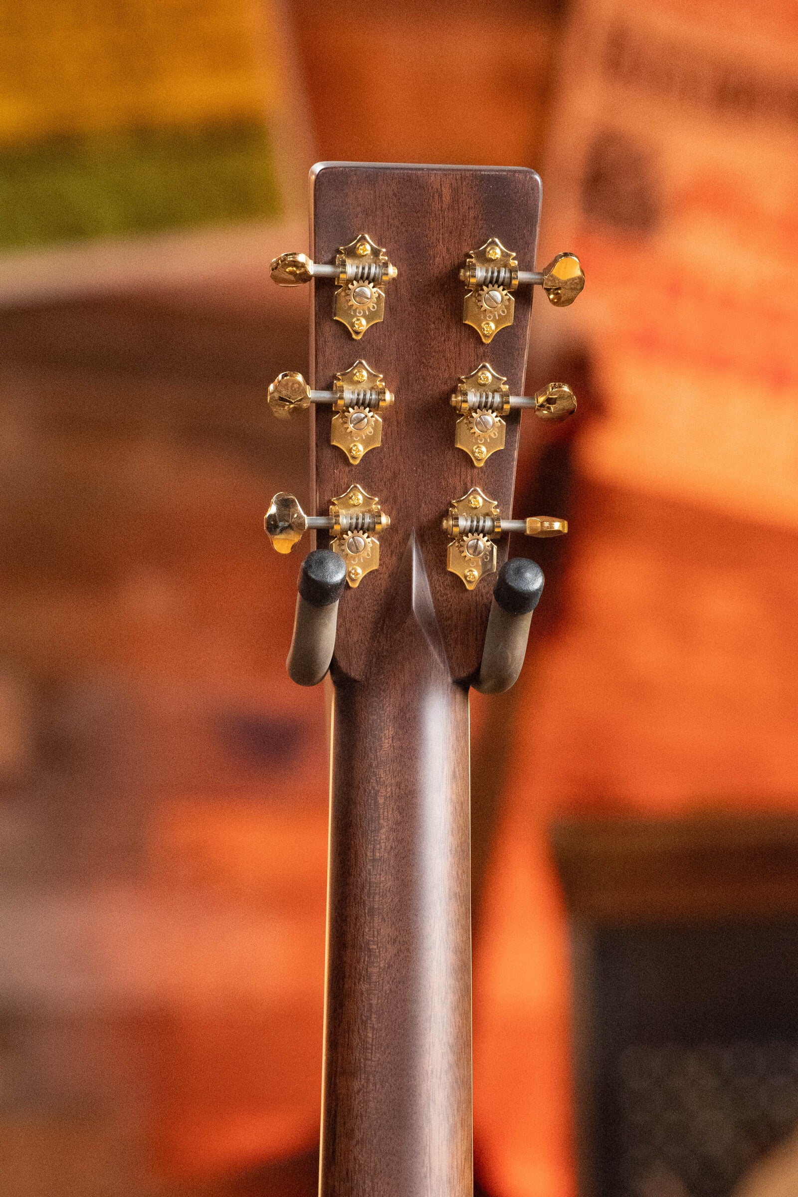 Close-up of the back of an Eastman Guitars E40D-TC-SB Thermo-cured Adirondack/Rosewood Sunburst Dreadnought Acoustic Guitar #1113 headstock with six gold tuners, on a stand, set against a blurred warm background. Rosewood adds rich visual appeal.