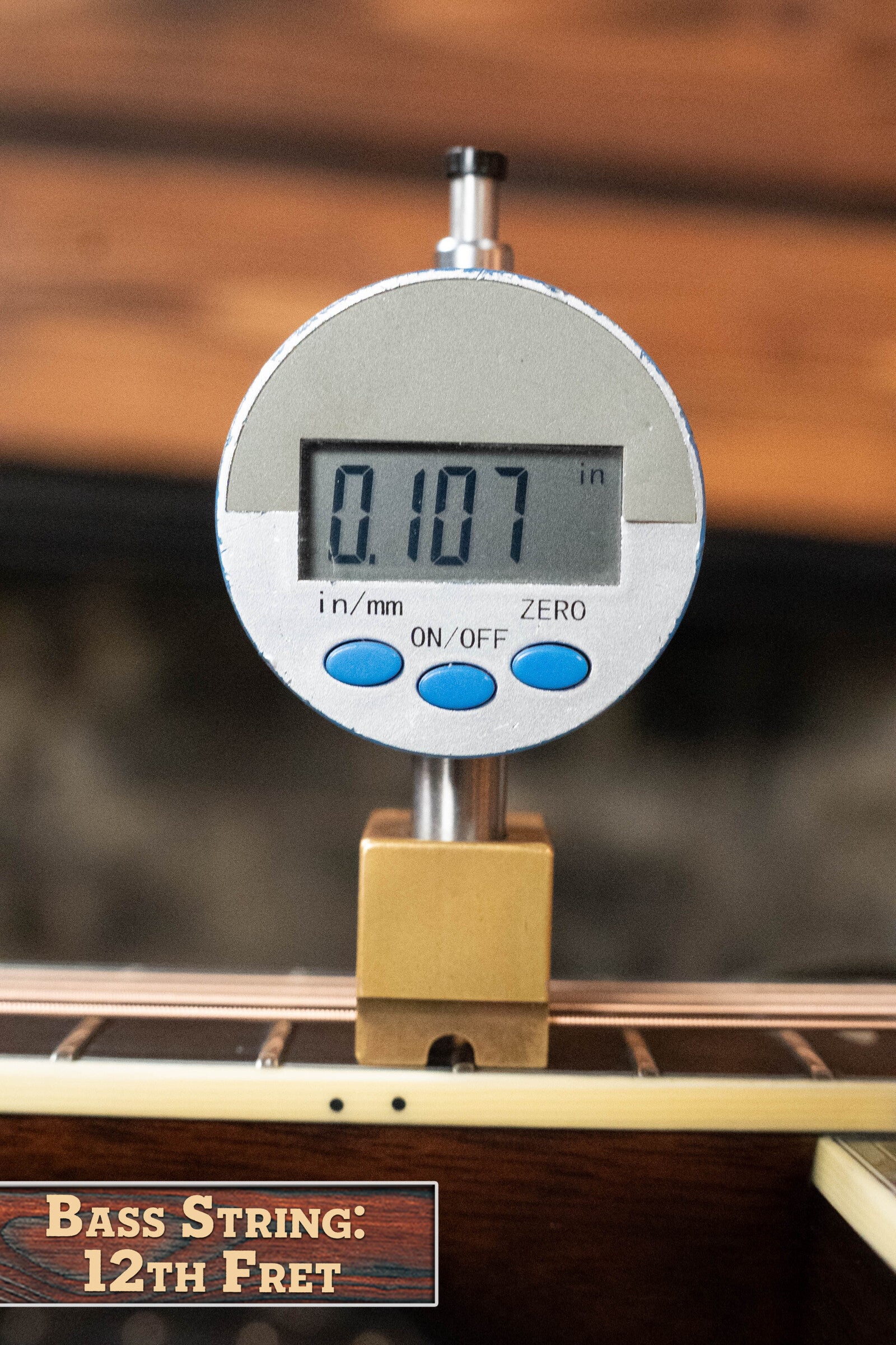 A digital caliper reads 0.107 inches while measuring a bass guitar string at the 12th fret, labeled “Bass String: 12th Fret,” showcasing precision similar to an Eastman Guitars E40D-TC-SB Sunburst Dreadnought (#1113) setup.