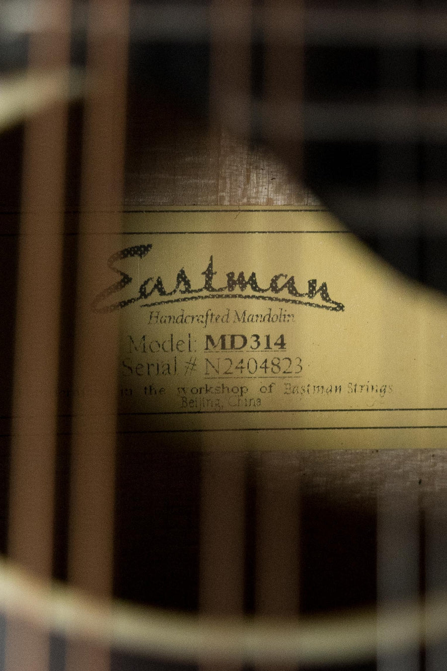 Close-up of a label inside the Eastman Guitars MD314 F-Style Oval Hole Mandolin #4823, visible through the strings and showing model and serial number.