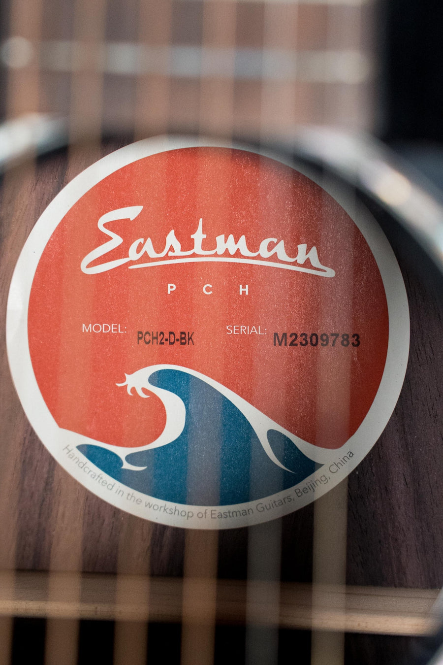 Eastman PCH2-D-BK acoustic guitar label showing model and wave design on black wood background. - Eastman PCH2-D-BK Solid Sitka/Laminated Rosewood Black Top Dreadnought Acoustic Guitar #9783 - Default Title