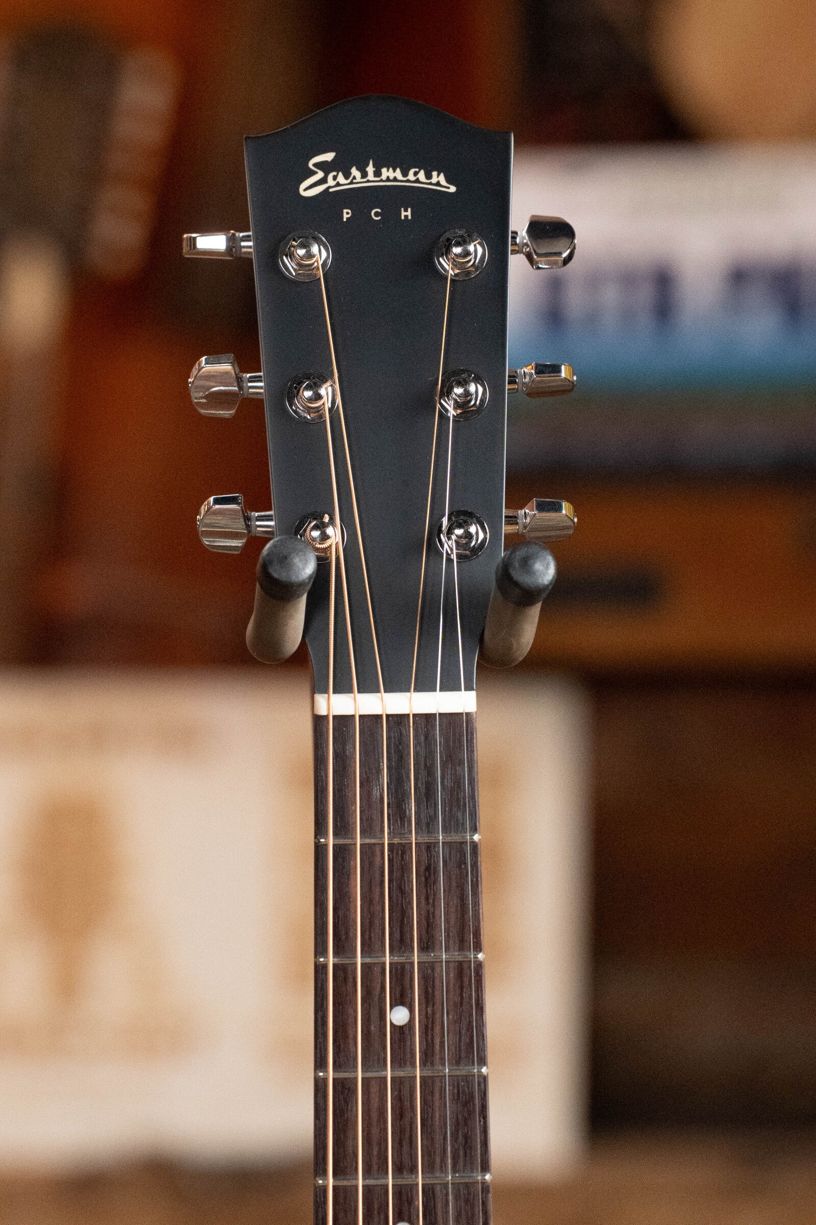 Close-up of the headstock of an Eastman Guitars PCH2-TG Thermo-Cured Solid Sitka/Laminated Rosewood Travel Acoustic Guitar #9714, showing six tuning pegs, visible strings, and the Eastman logo on the black headstock. Blurred background.