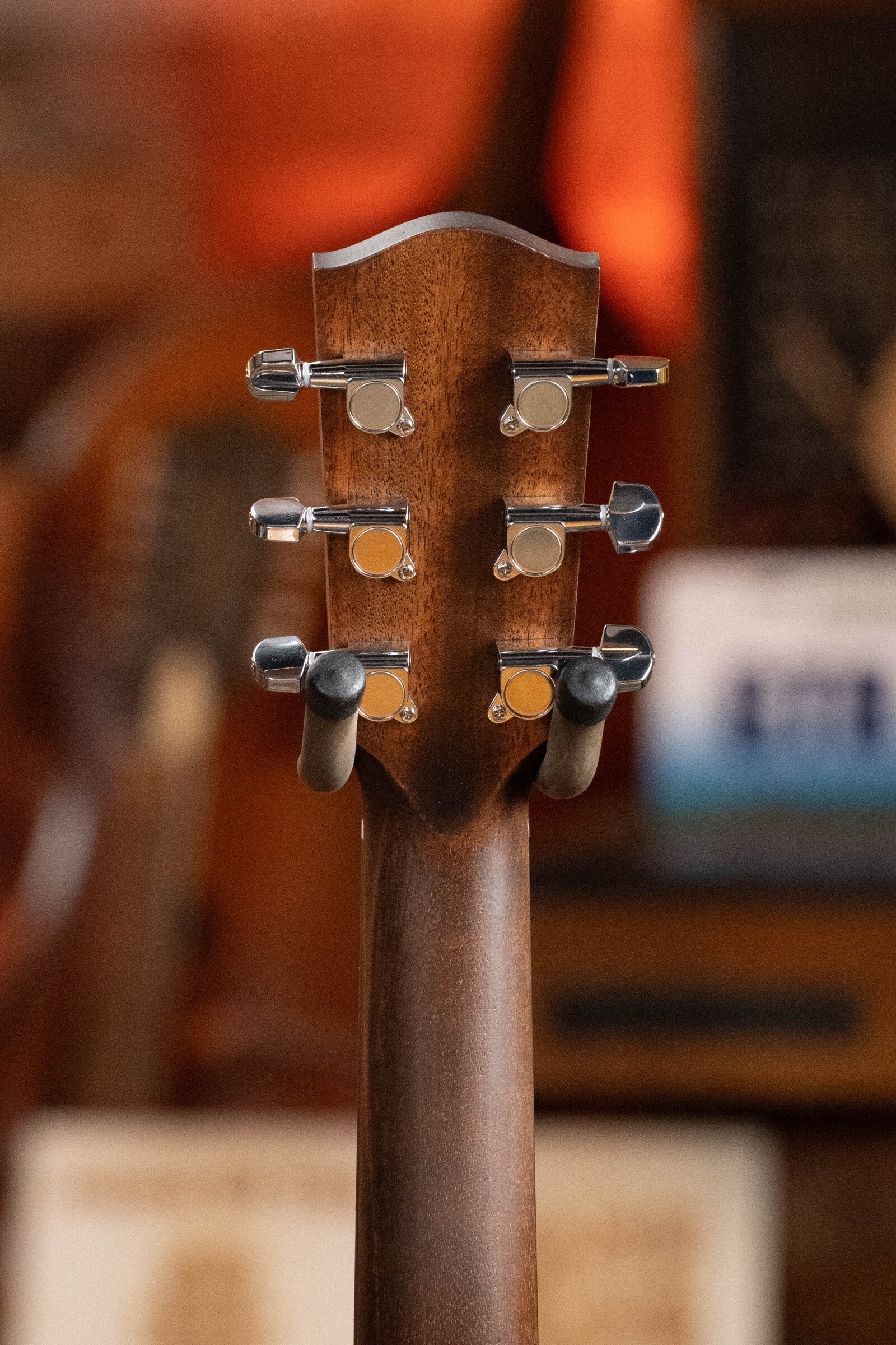 Close-up of the back of an Eastman PCH2-TG Travel Acoustic Guitar #9714 by Eastman Guitars, featuring six silver tuning pegs on a laminated rosewood neck against a blurred, warm-toned background.