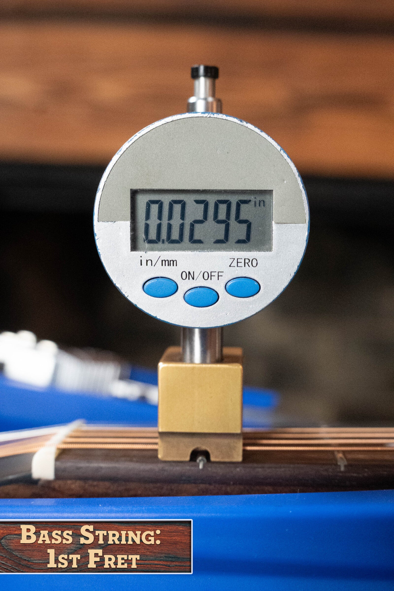 A digital caliper reads 0.0295 inches, measuring bass string height at the 1st fret. A label says, “Bass String: 1st Fret,” next to an Eastman Guitars PCH2-TG Thermo-Cured Solid Sitka/Laminated Rosewood Travel Acoustic Guitar #9714.