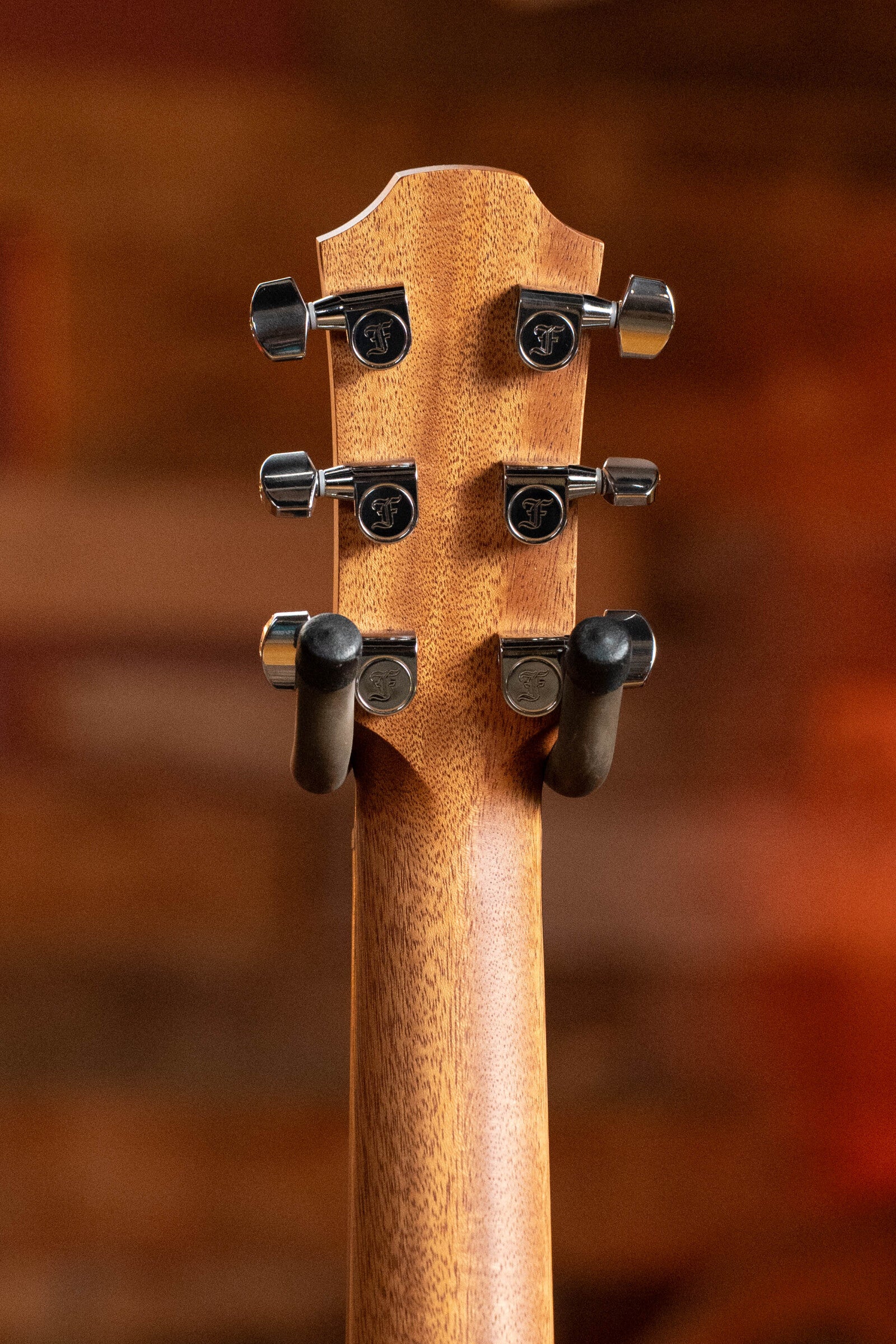 Close-up of the Furch Pioneer-ER VTC Cutaway Travel Guitar headstock, highlighting tuning pegs and wooden neck, set against a blurred warm-toned background.