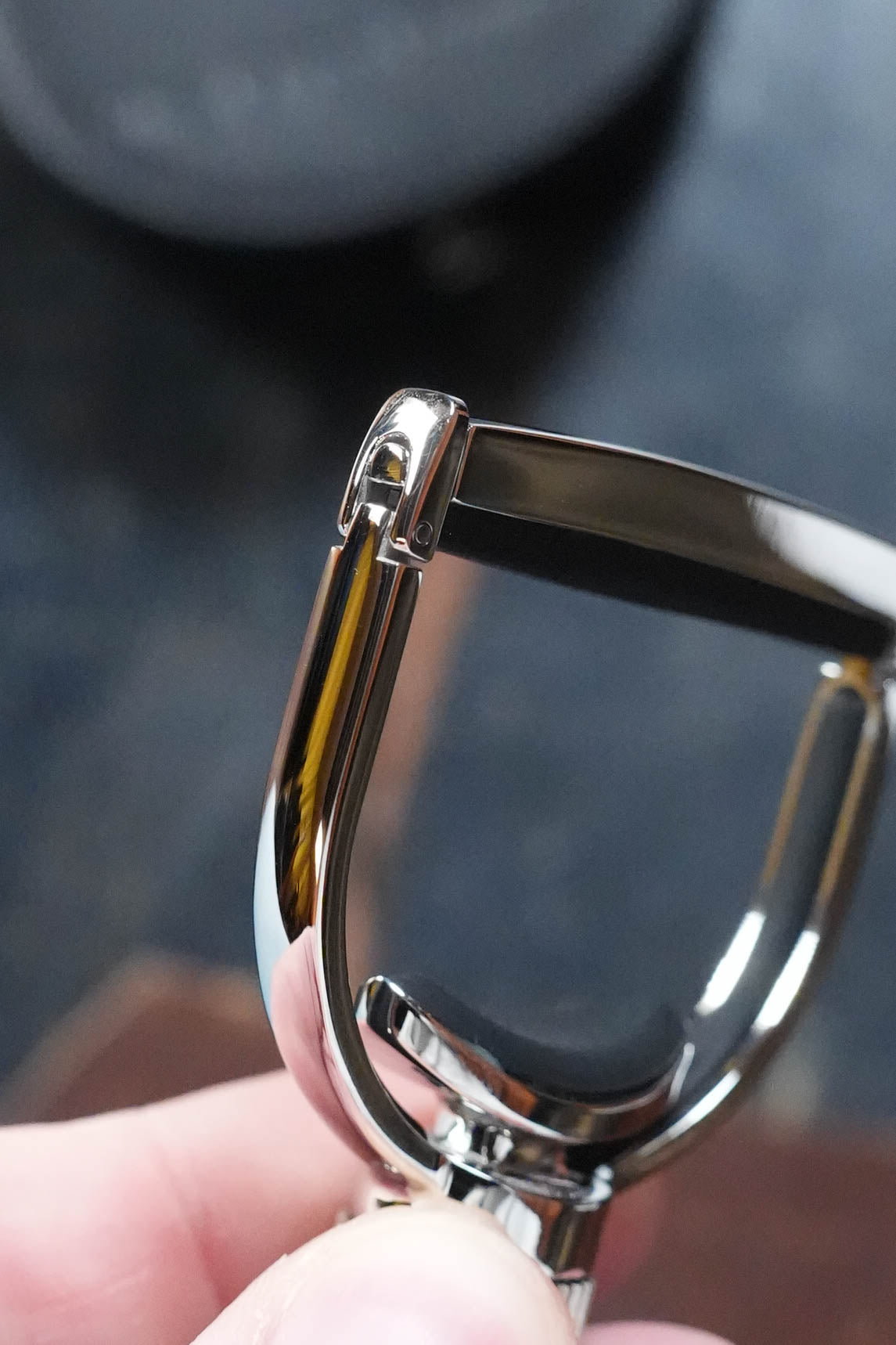 A close-up of a shiny metal peeler held by a hand showcases its blade and curved handle, echoing the sleek design of The Acoustic Shoppe G7th Heritage Banjo Capo S1 Standard Neck Width, against a blurred dark background.