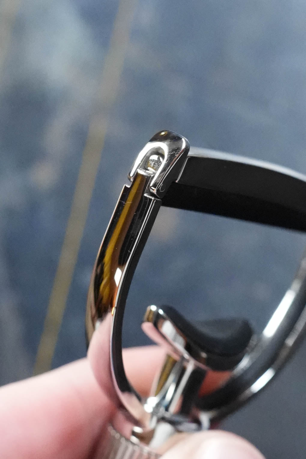 A close-up of the G7th Heritage Banjo Capo S1 Wide by The Acoustic Shoppe, with its precise clamp and sleek design in focus—reminiscent of a metal eyelash curler—set against a softly blurred background.