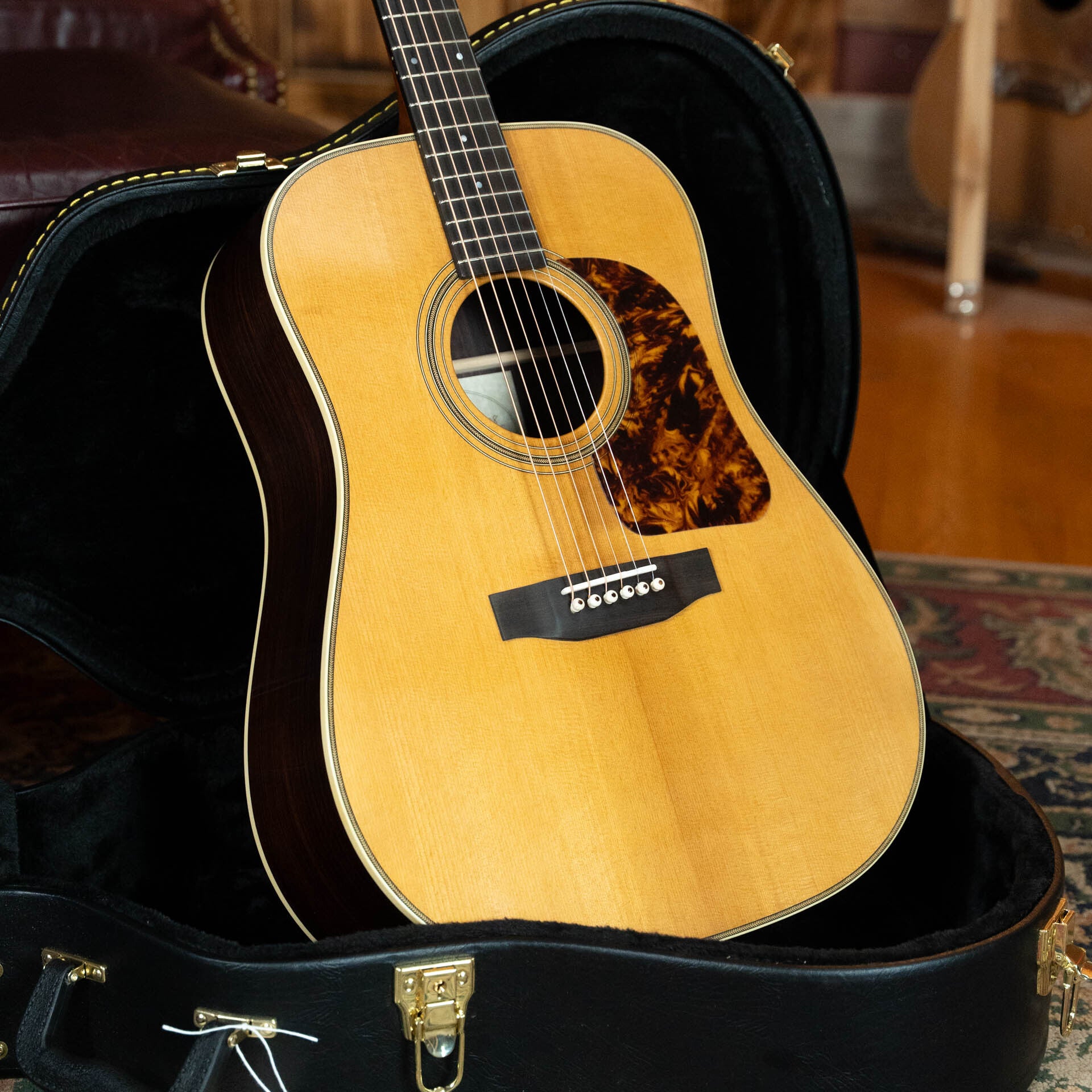 A Gallagher Guitar Co. The Bluegrass Bell Torrefied Adirondack/Rosewood Dreadnought Acoustic Guitar #4408 with a light top, dark sides, and tortoiseshell pickguard rests in an open black case on a patterned rug.