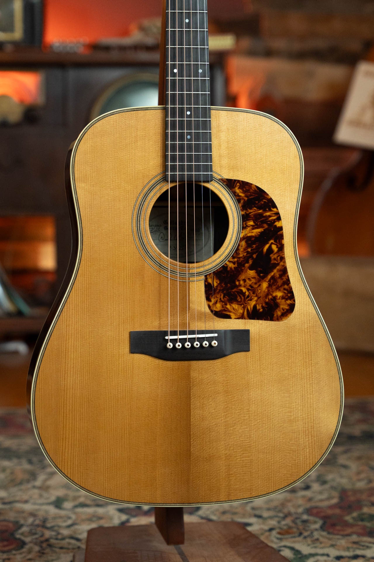 A close-up of the Gallagher Guitar Co. The Bluegrass Bell Torrefied Adirondack/Rosewood Dreadnought Acoustic Guitar #4408, featuring a natural wood finish, Adirondack spruce top, dark tortoiseshell pickguard, and six strings on a stand indoors.