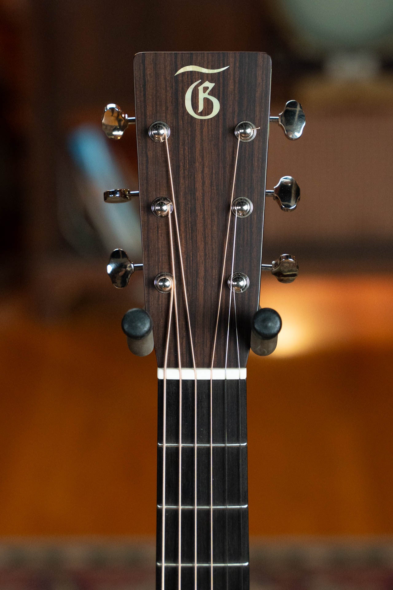 Close-up of the headstock of the Gallagher The Bluegrass Bell Torrefied Adirondack/Rosewood Dreadnought Acoustic Guitar #4408 by Gallagher Guitar Co., showing six tuning pegs, strings, and neck against a blurred indoor background.