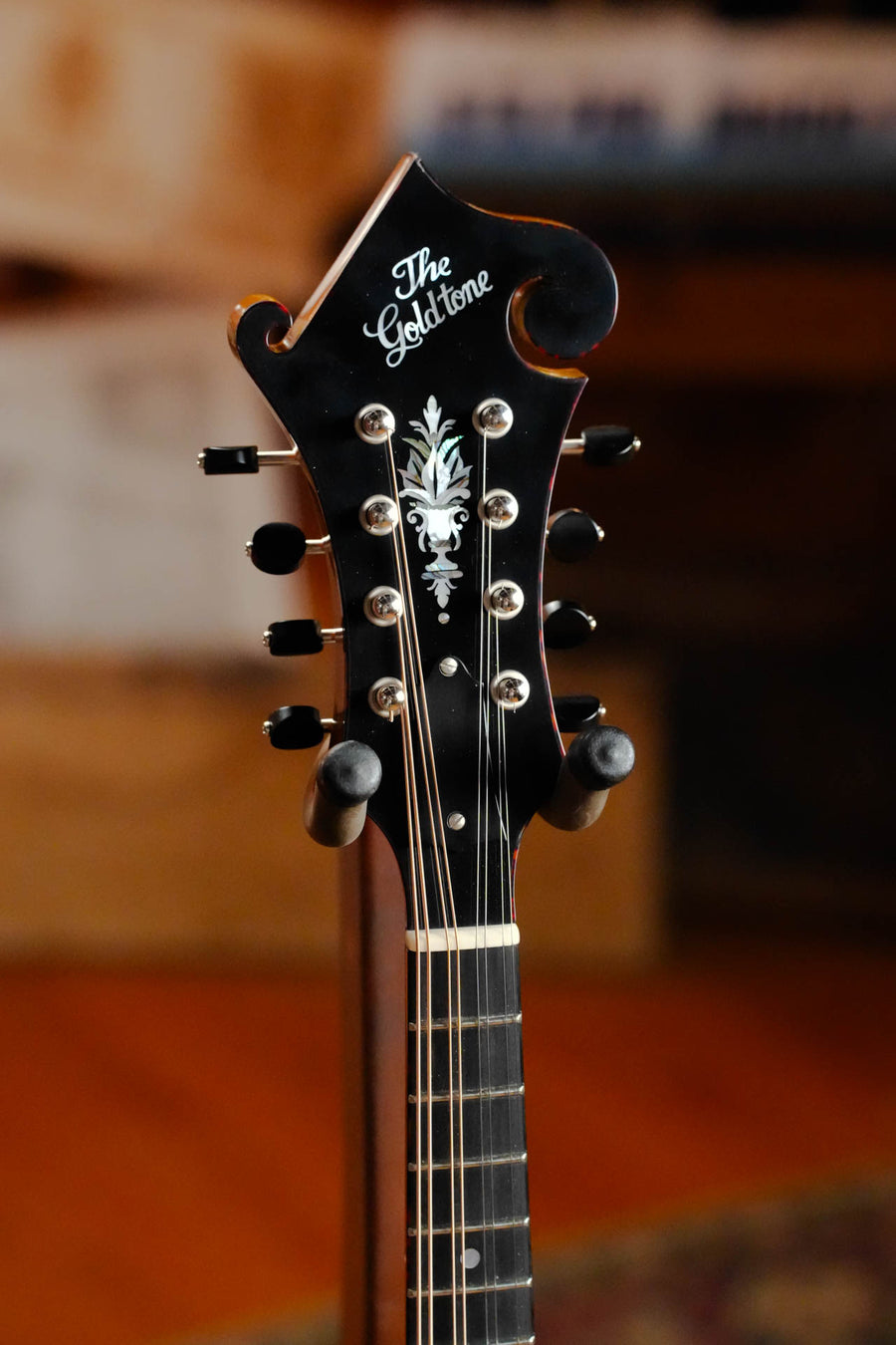 Close-up of the Gold Tone Grandmaster Mandolin Elite - Honey Amber Finish #5627 headstock, featuring decorative inlay and tuning pegs. Crafted from premium tonewoods, its beauty is highlighted against a softly blurred background.