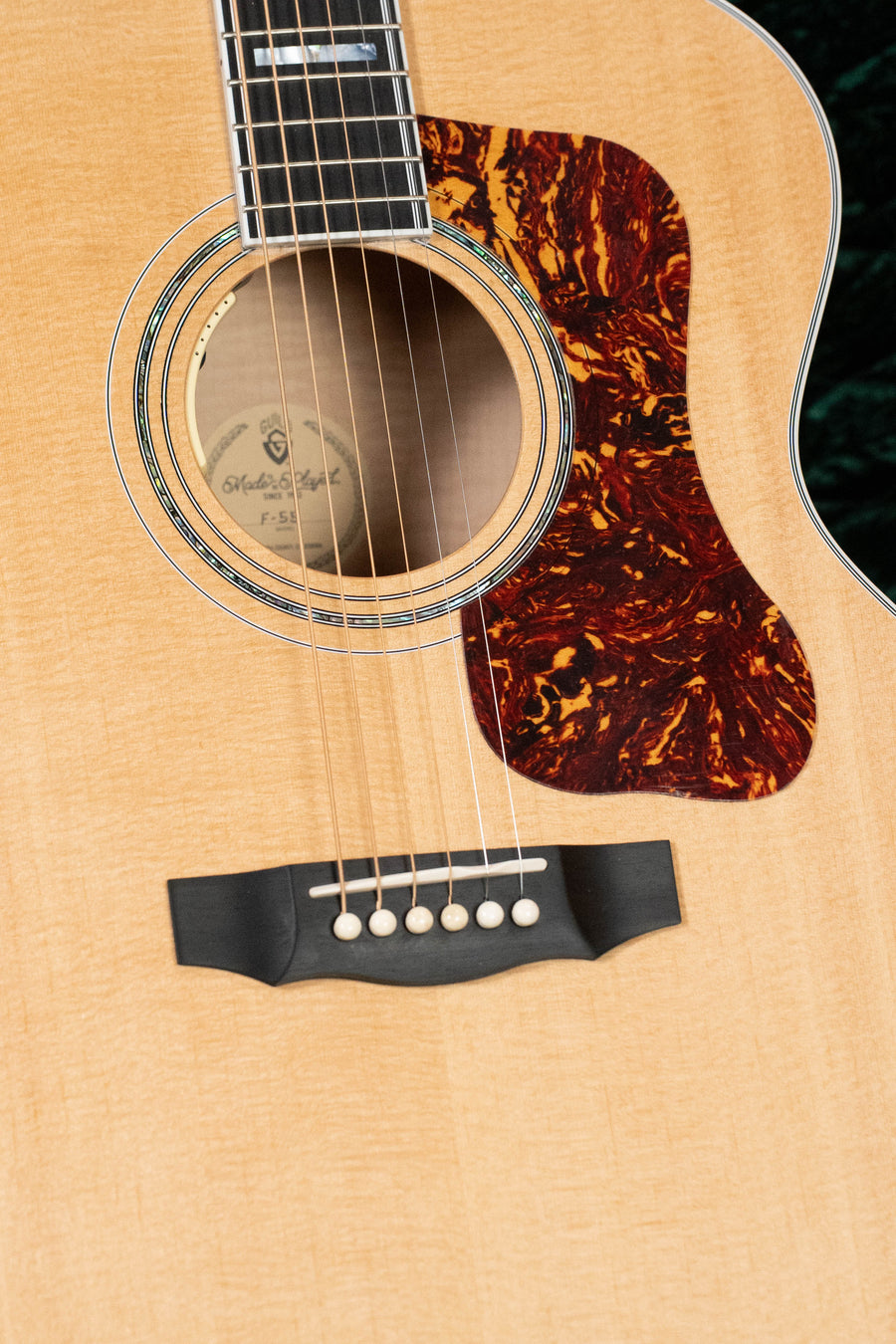Close-up of a Guild Guitars F-55E Sitka/Maple Jumbo Natural Gloss (#0842) body, showing the sound hole, marbled pickguard, bridge, and six strings. Features LR Baggs Anthem electronics and a natural wood finish.