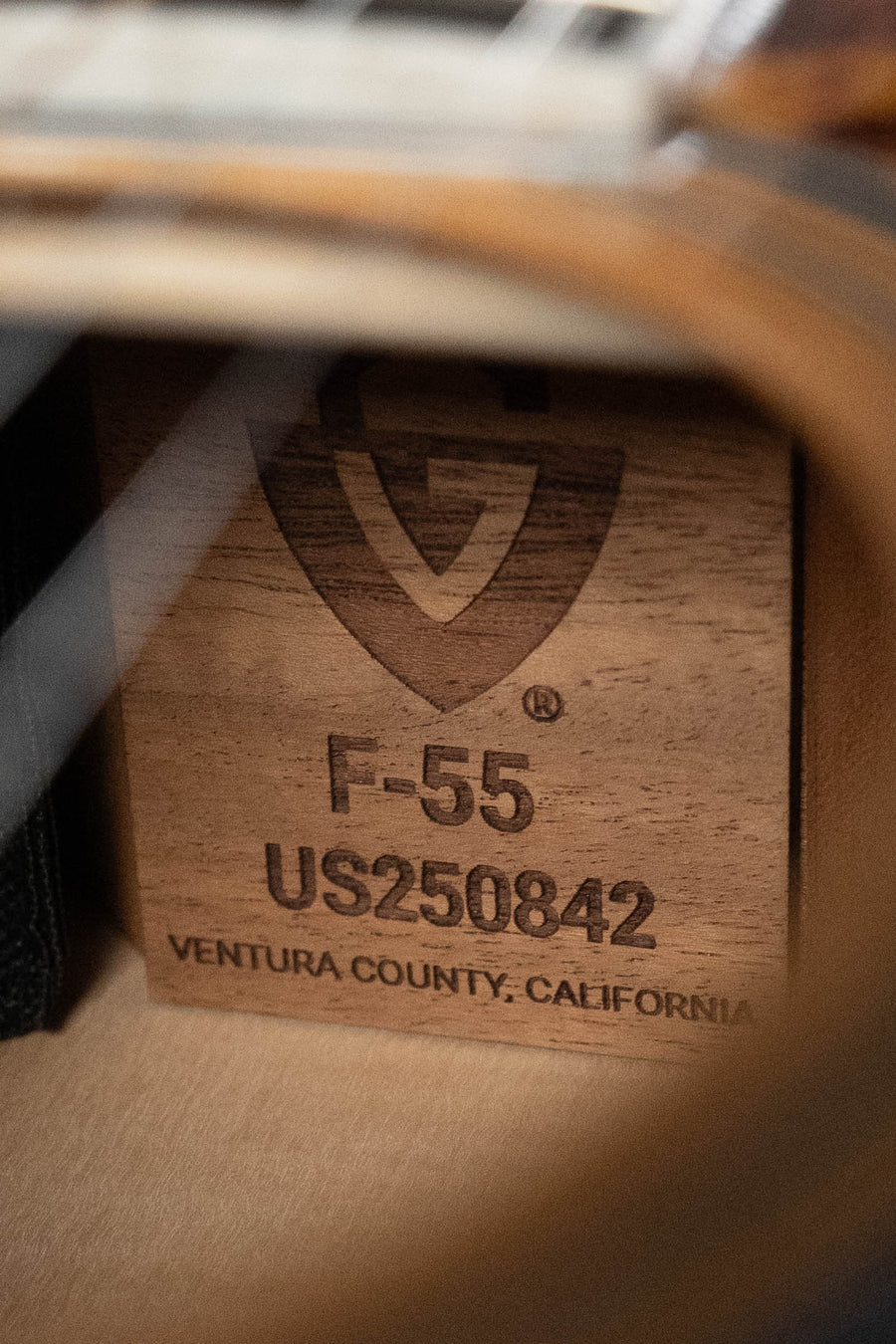 Close-up of a wooden Guild Guitars F-55E Sitka/Maple Jumbo Natural Gloss label inside the acoustic guitar, showing a shield logo, model F-55E, serial #0842, and Ventura County, California.