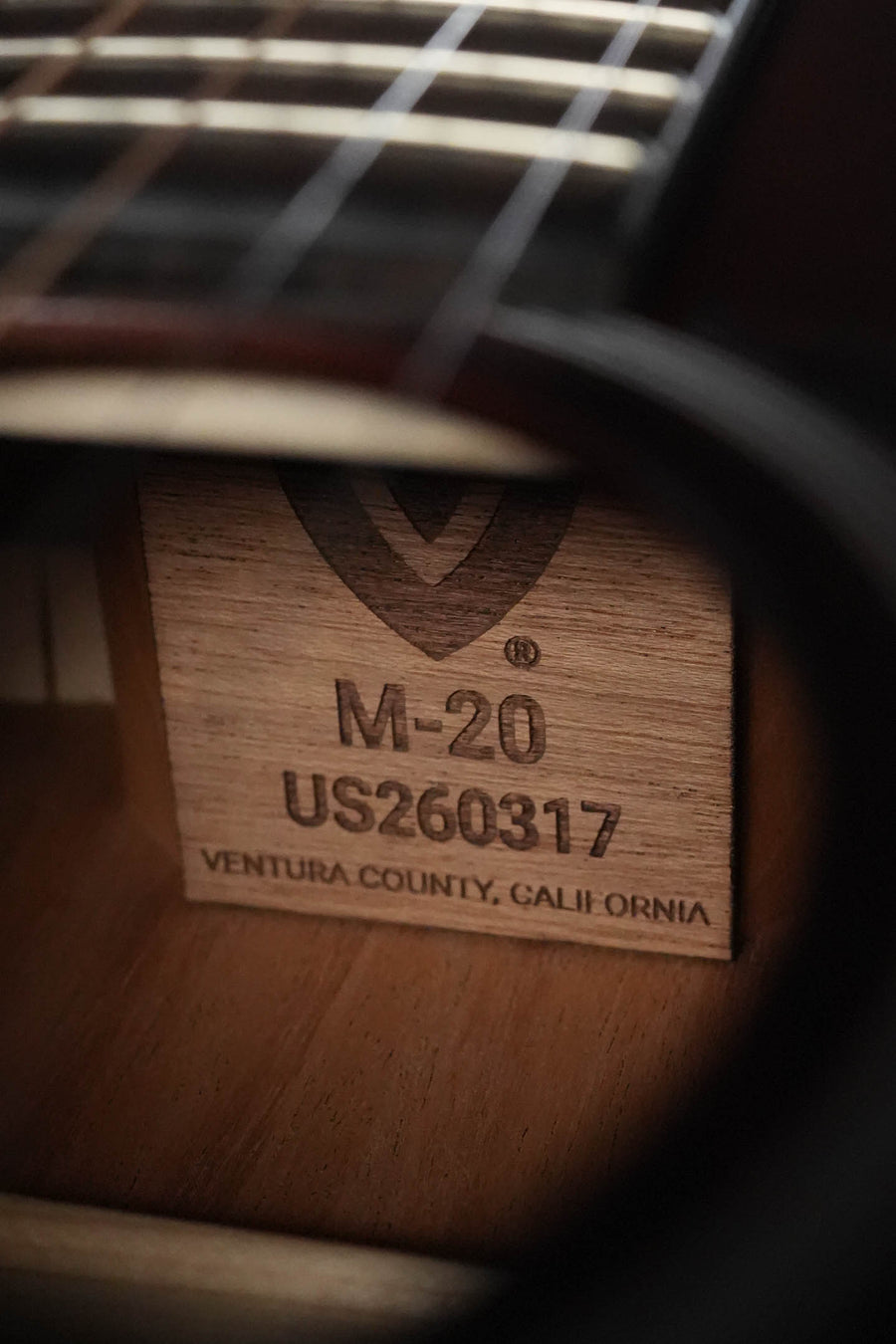 Close-up of the Guild Guitars M-20 Natural All African Mahogany Concert Acoustic Guitar (#0317) interior label, visible through the sound hole beneath the strings and fretboard.