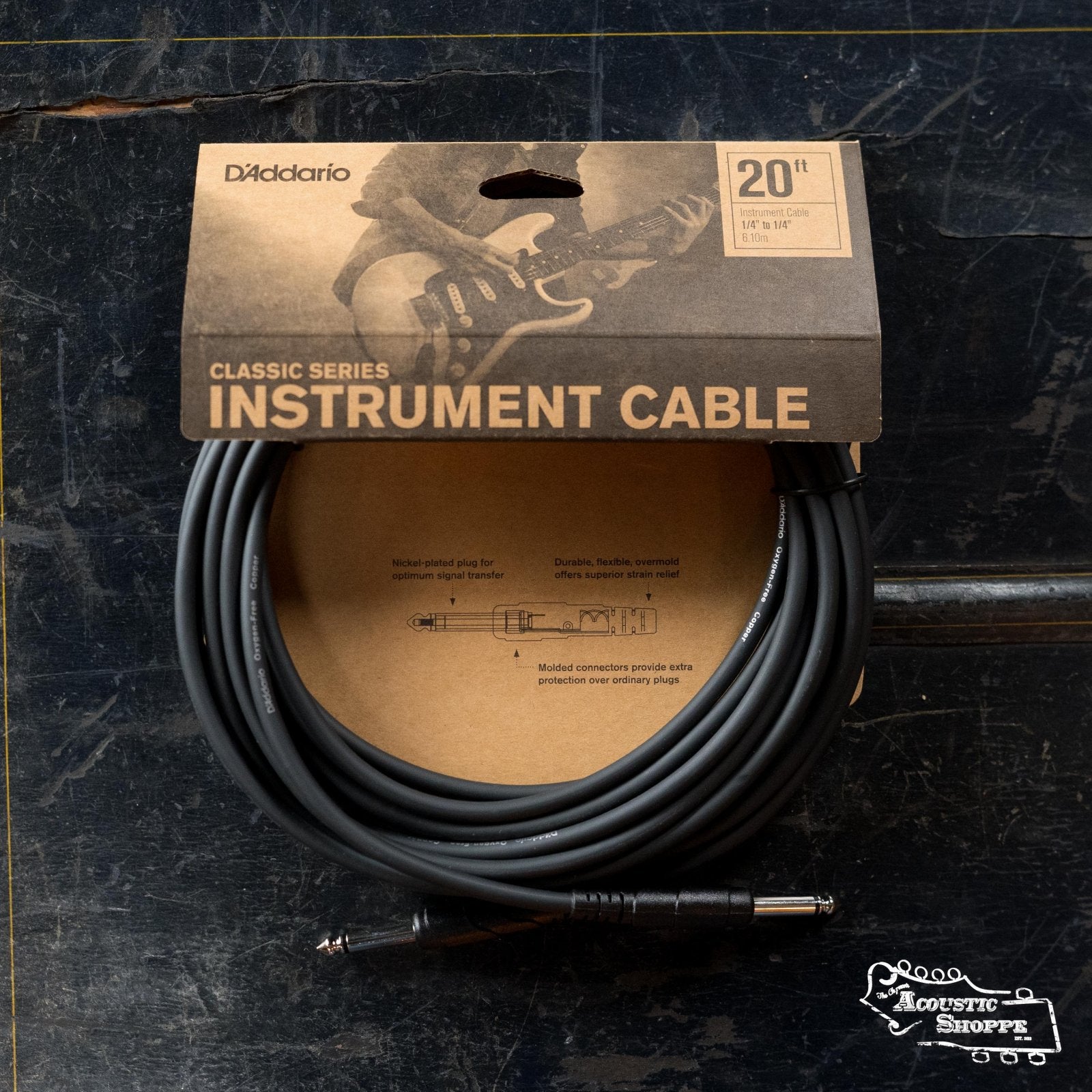 A 20-foot D'Addario PW-CGT Classic Series Instrument Cable (Straight to Straight), made with oxygen-free copper for top signal quality, is displayed in its box on a dark surface. The packaging shows a guitarist image and product details.