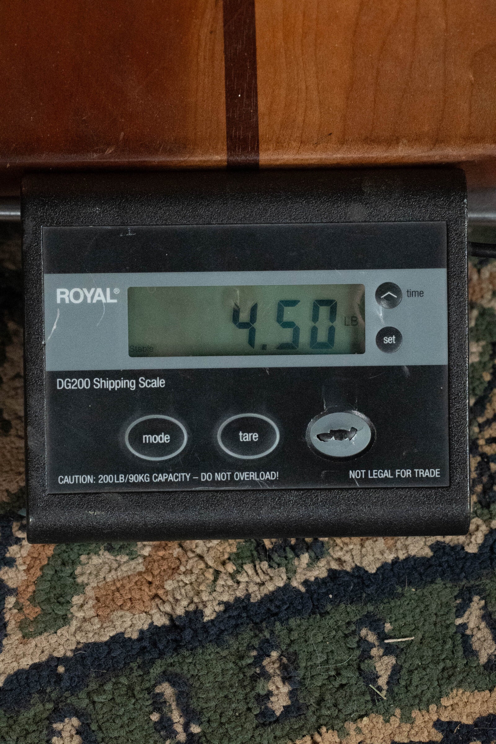 A digital shipping scale shows 4.50 pounds as it weighs the Martin & Co. *Limited Edition* CEO-11 European Spruce/White Oak New Horizons Blue Burst Grand Auditorium Guitar w/Electronics #1204 on a patterned carpet beside a wooden surface.