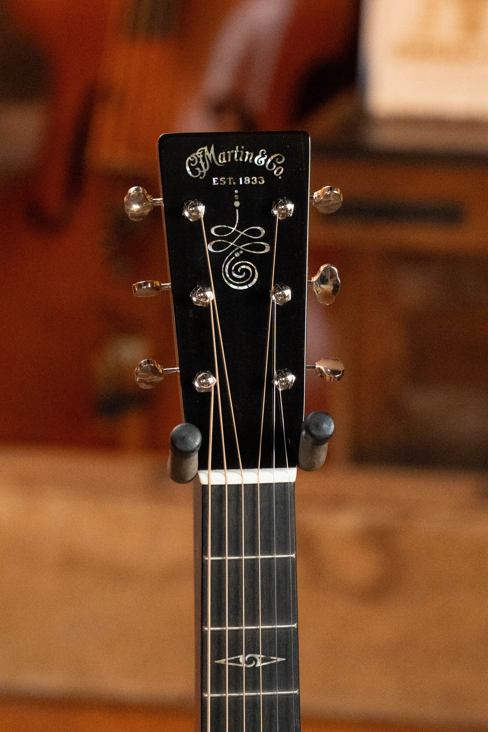 Close-up of the Martin & Co. *Limited Edition* CEO-11 Grand Auditorium Guitar (#1204) headstock, featuring tuning pegs and logo, set against a warm, blurred wooden background. European Spruce/White Oak New Horizons Blue Burst finish with electronics.