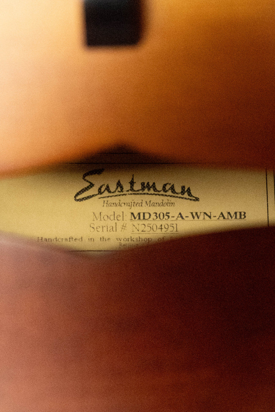 A close-up through the sound hole of an Eastman Guitars MD305 shows a label with its logo and serial info. Warm wood tones highlight this pre-order 2026 Wide Nut Adirondack/Maple A-Style mandolin.