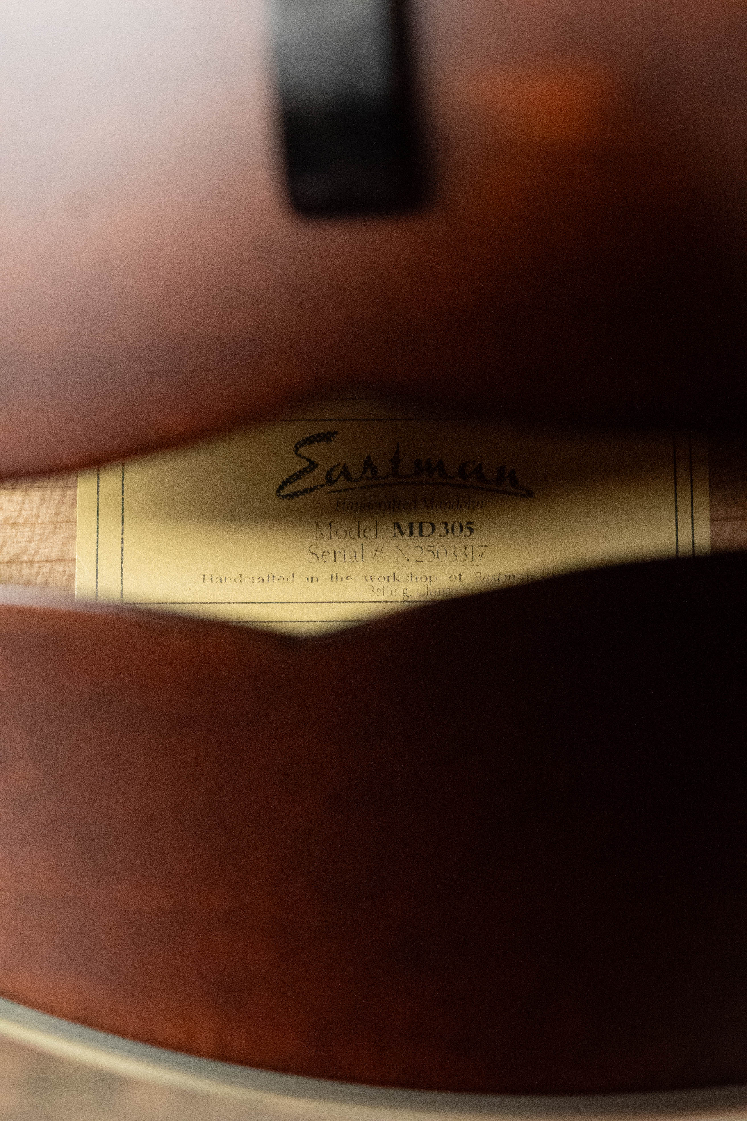 Close-up of a label inside an Eastman Guitars MD305 Spruce/Maple A-Style Hand-Carved Mandolin #3317, partially seen beneath the solid spruce top and wooden body.