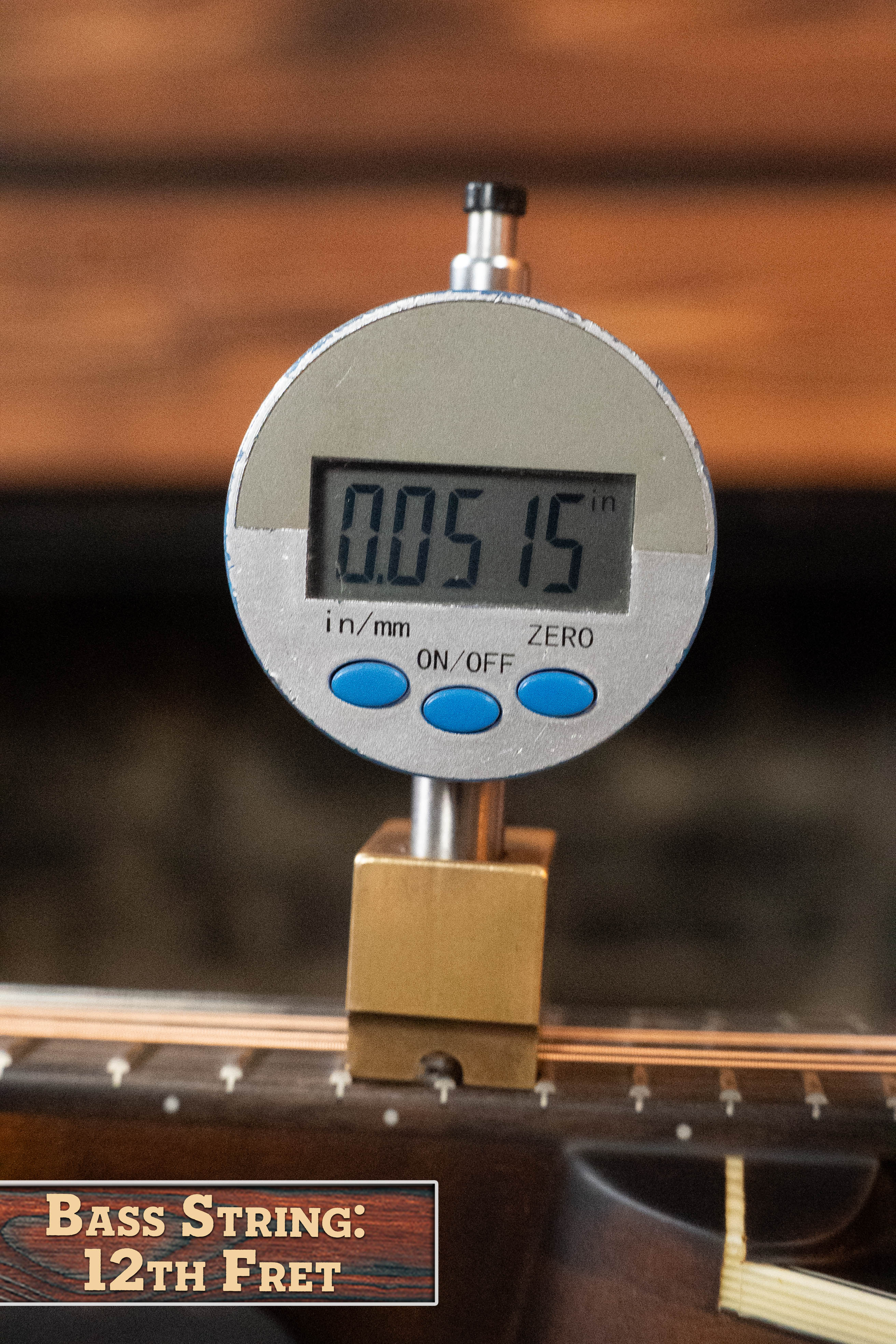 A digital gauge, held by a gold clamp on the neck of an Eastman MD305 Spruce/Maple A-Style Hand-Carved Mandolin (#3596) by Eastman Guitars, reads 0.0515 inches above the carved top at the bass string’s 12th fret.