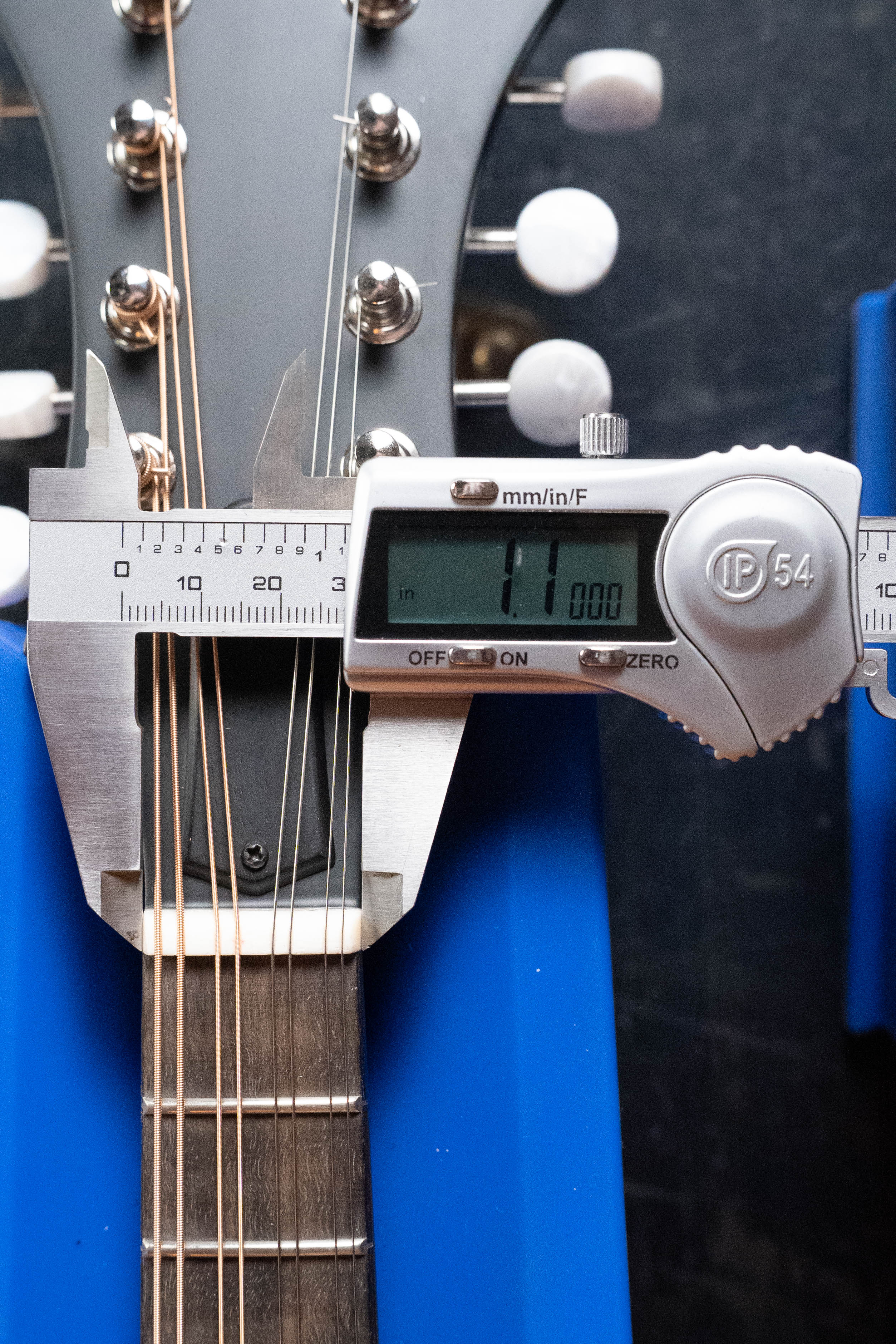 A digital caliper shows 1.1 inches (28 mm) as it measures the neck width near the headstock of an Eastman MD315 F-Style Hand-Carved Mandolin #0917 by Eastman Guitars, which rests on a blue support.