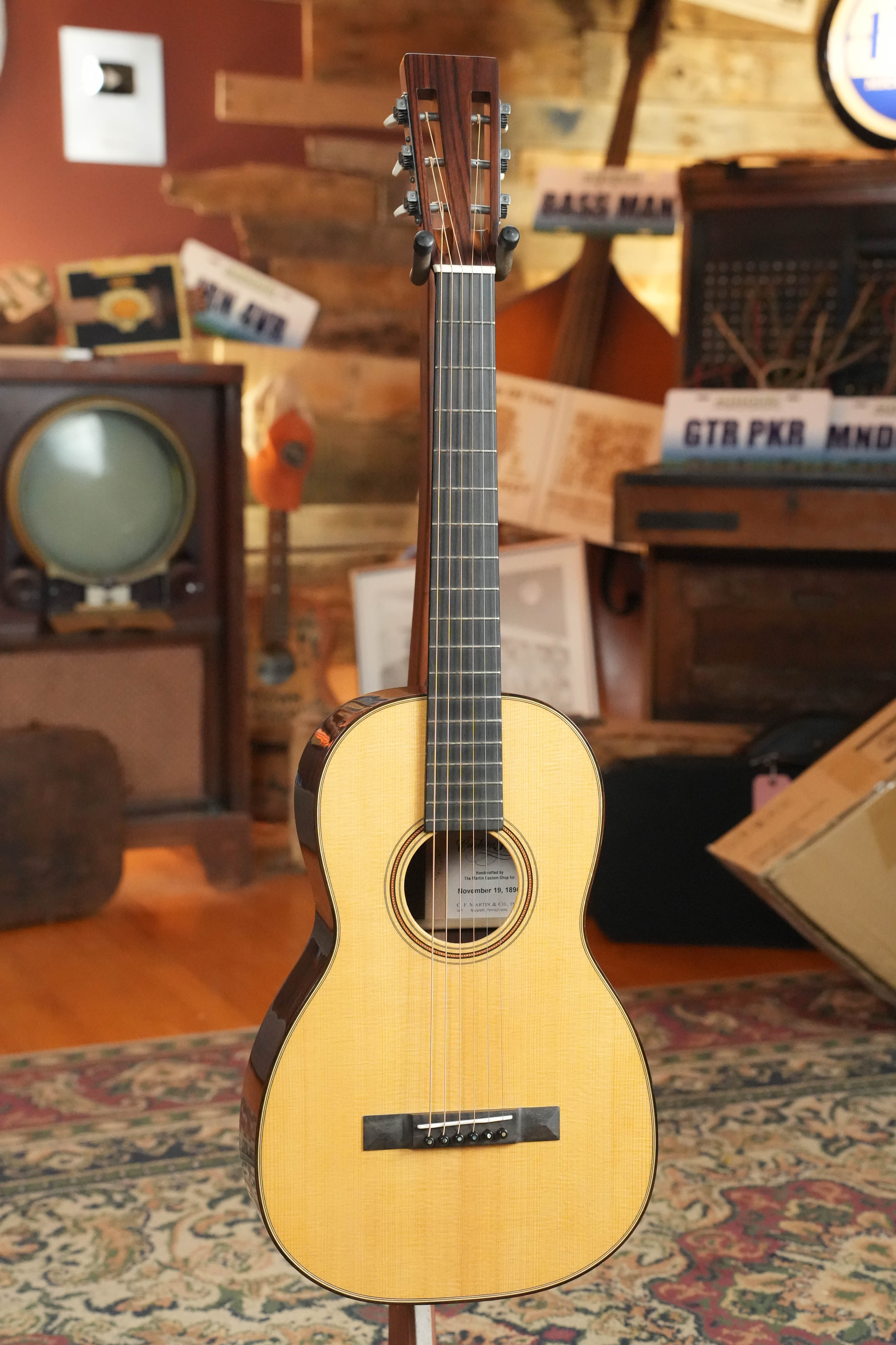 The Martin & Co. Custom Shop Sitka/Rosewood Acoustic Guitar #6904 stands on a colorful patterned rug in a room decorated with musical instruments, retro electronics, and old license plates.