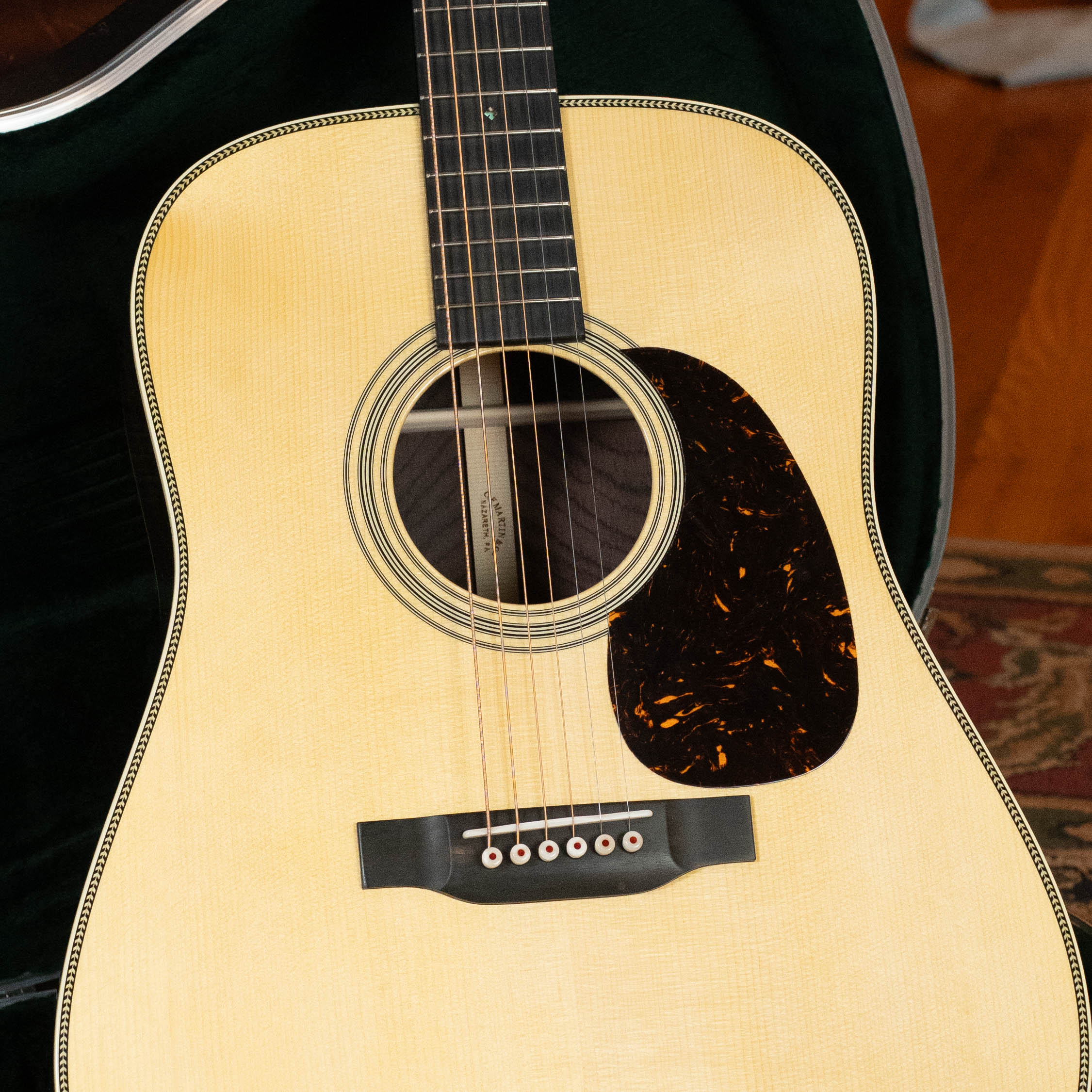 A close-up of the Martin & Co. Custom Shop HD-28 Style Spruce/Wild Grain Rosewood Custom "D" Dreadnought Acoustic Guitar #7410 highlights its light Adirondack spruce top, dark pickguard, six strings, and fretboard, with a rug and guitar in the background.