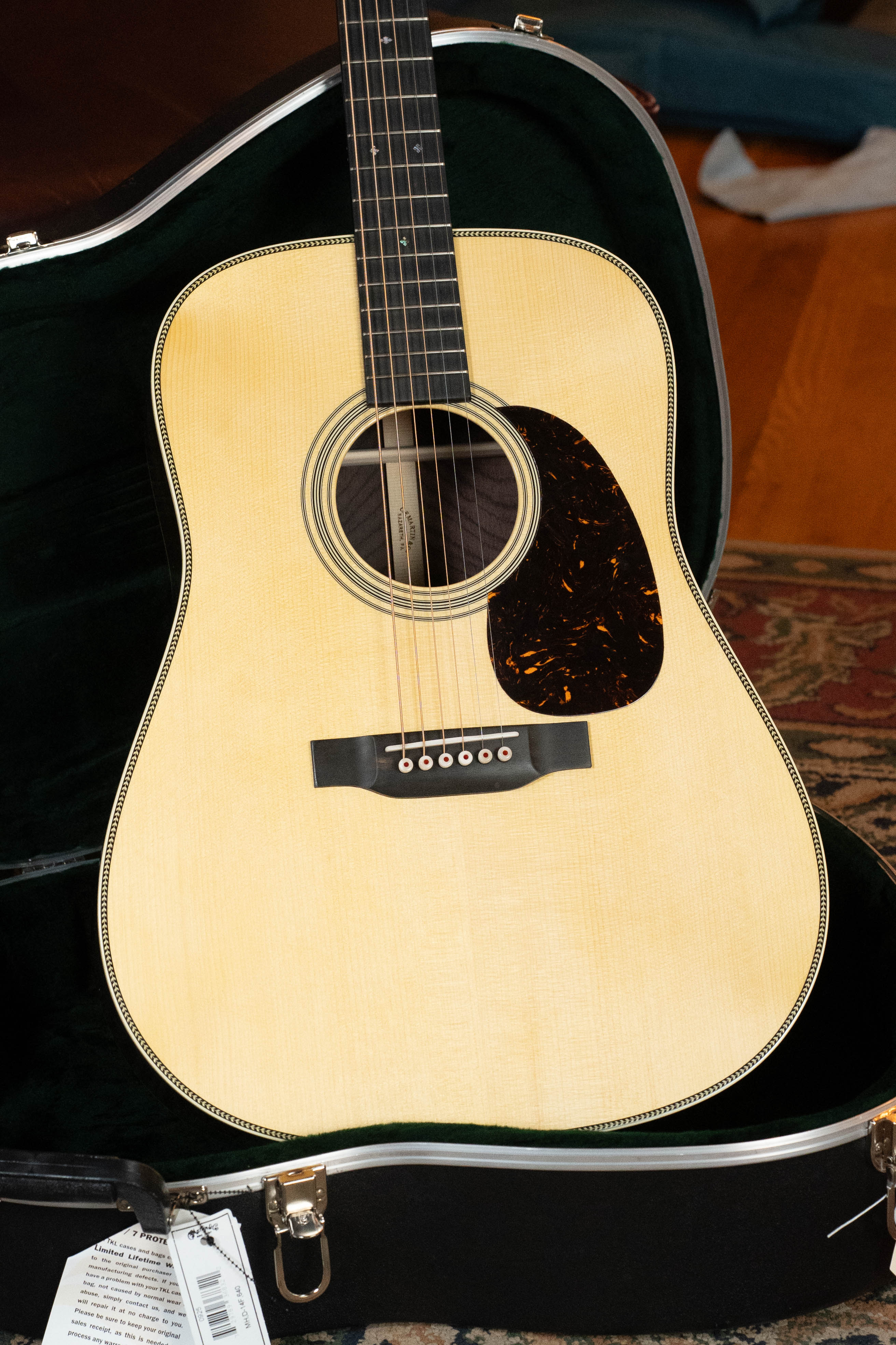 A Martin & Co. Custom Shop HD-28 Style Spruce/Wild Grain Rosewood "D" Dreadnought Acoustic Guitar (#7410) with an Adirondack spruce top and tortoiseshell pickguard rests in an open black case on a wooden floor near a patterned rug.