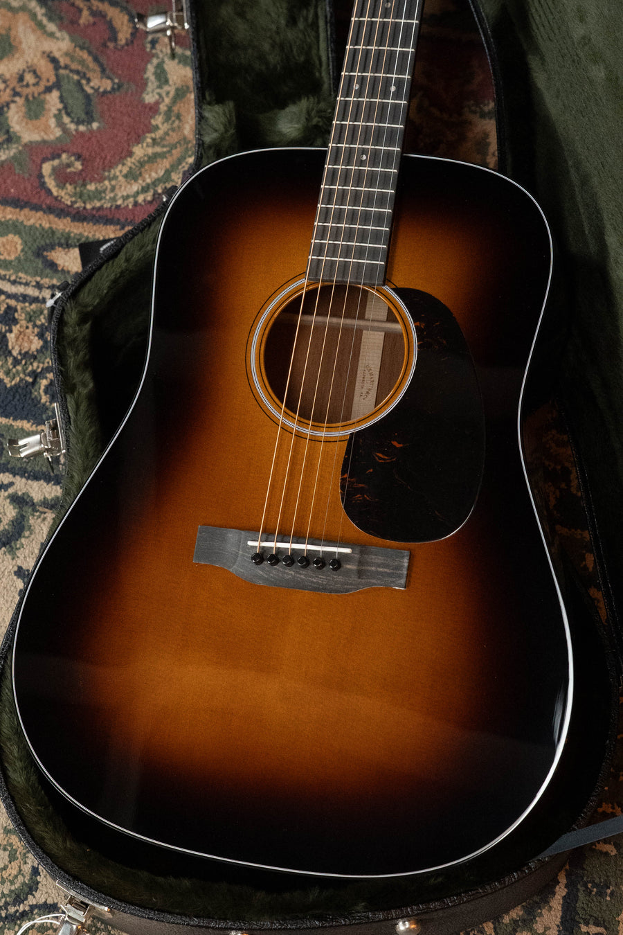 A Martin & Co. D-18 Spruce/Mahogany 1935 Gloss Sunburst Finish Dreadnought Acoustic Guitar #2409 rests inside an open lined case on a patterned rug, featuring a dark gloss finish and round soundhole.