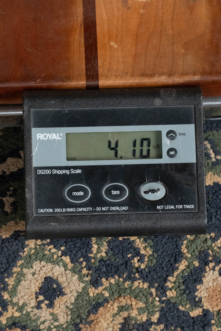 A digital shipping scale on a patterned carpet shows 4.10 pounds—the ideal way to weigh your Martin & Co. D-18 Spruce/Mahogany 1935 Gloss Sunburst Finish Dreadnought Acoustic Guitar #2409 before shipping. The black device has gray buttons and capacity warnings.
