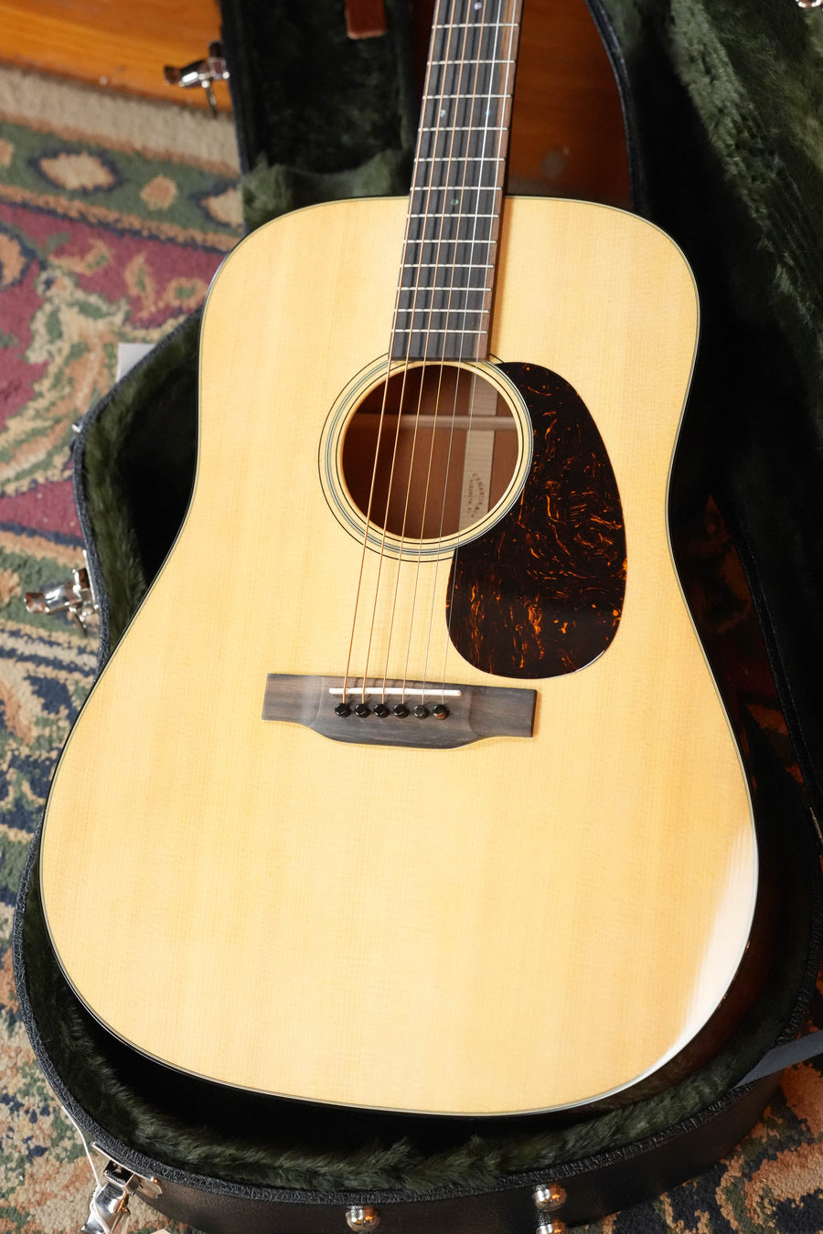 A Martin & Co. D-18 Spruce/Mahogany Gloss Finish Dreadnought Acoustic Guitar #5420 with a natural finish sits in an open, green-lined hard case atop a colorful patterned rug.