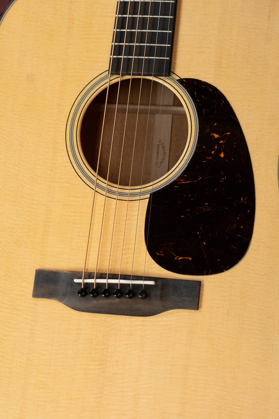 Close-up of the Martin & Co. D-18 Spruce/Mahogany Satin Finish Dreadnought Acoustic Guitar #1864, featuring its wooden soundboard, strings, black pickguard, sound hole, mahogany back and sides, and part of the fretboard.