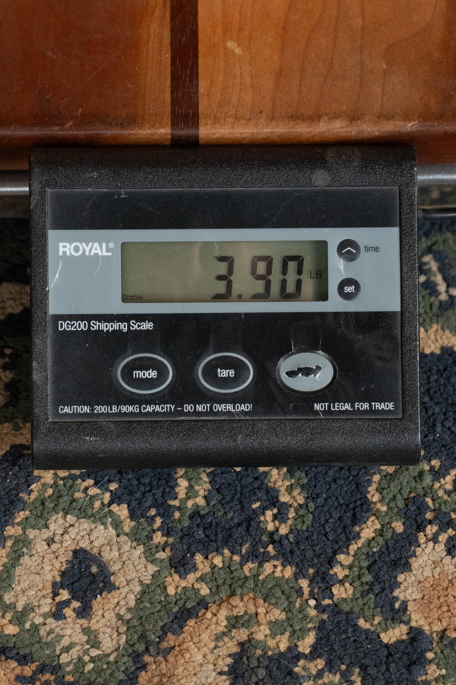 A digital shipping scale on a patterned carpet shows 3.90 lbs—ideal for shipping a Martin & Co. D-18 Spruce/Mahogany Satin Finish Dreadnought Acoustic Guitar #1864. The ROYAL DG200 Shipping Scale has multiple buttons and caution warnings visible.