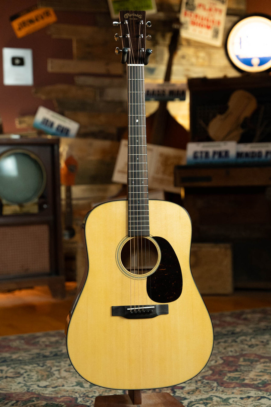 A Martin & Co. D-18 Spruce/Mahogany Gloss Finish Dreadnought Acoustic Guitar #9103 stands upright in a cozy vintage room with wooden walls, retro signs, an old TV, and warm ambient lighting.
