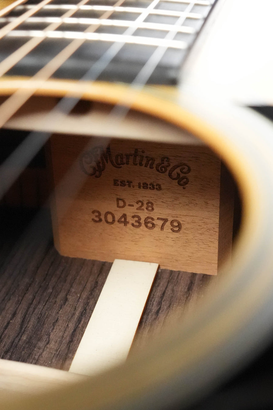 A close-up through the soundhole of the Martin & Co. D-28 Satin Spruce/Rosewood Acoustic Guitar #3679 reveals its label, with strings and fretboard of this rosewood dreadnought guitar visible above.