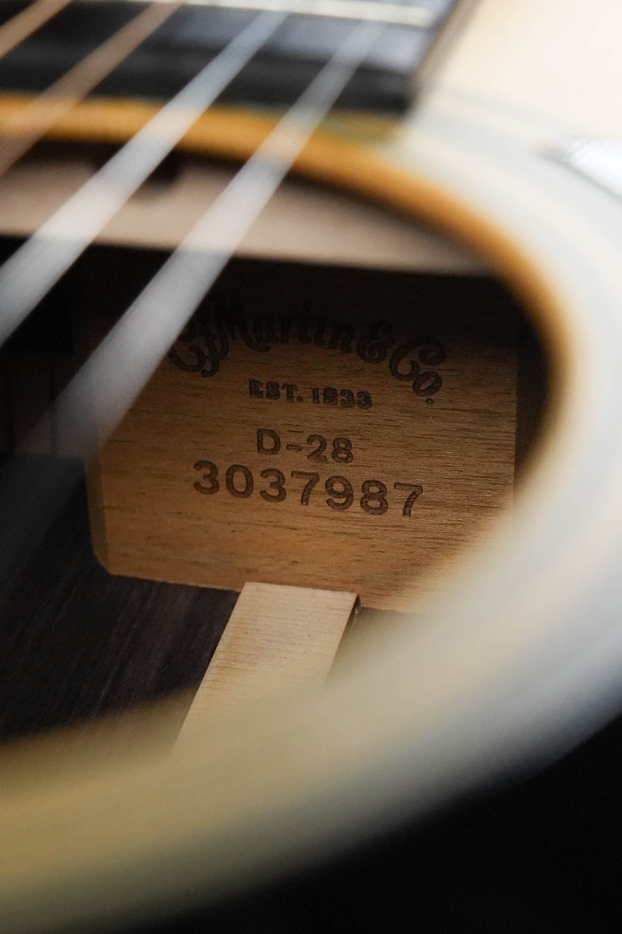 Close-up of the inside label of a Martin & Co. D-28 Satin Spruce/Rosewood Acoustic Guitar #7987, visible through the strings and sound hole.