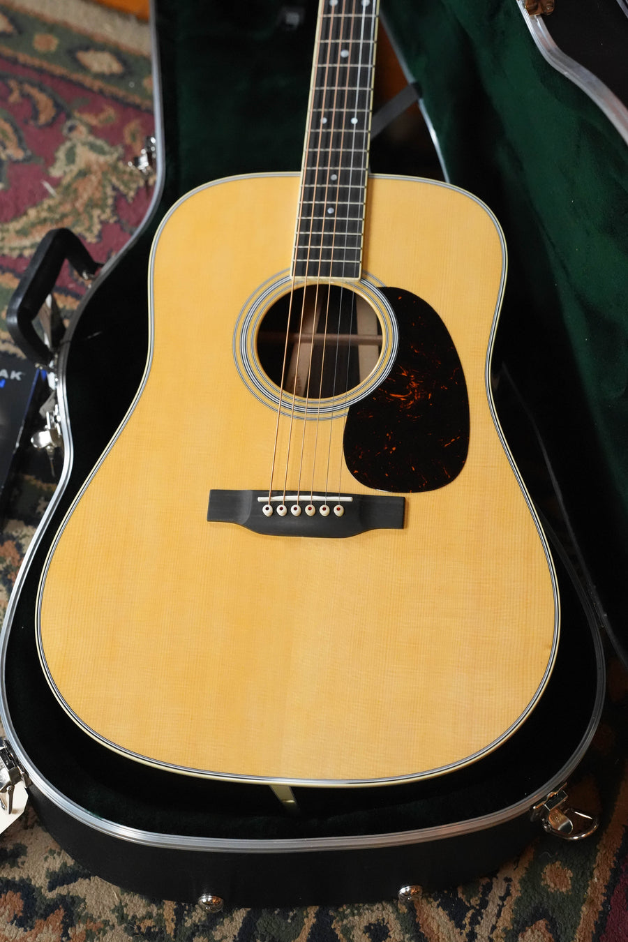 A Martin & Co. D-35 Gloss Aging Toner Dreadnought Acoustic Guitar (#2597) with a light wood body and dark pickguard is shown in an open black hard case on a patterned rug.