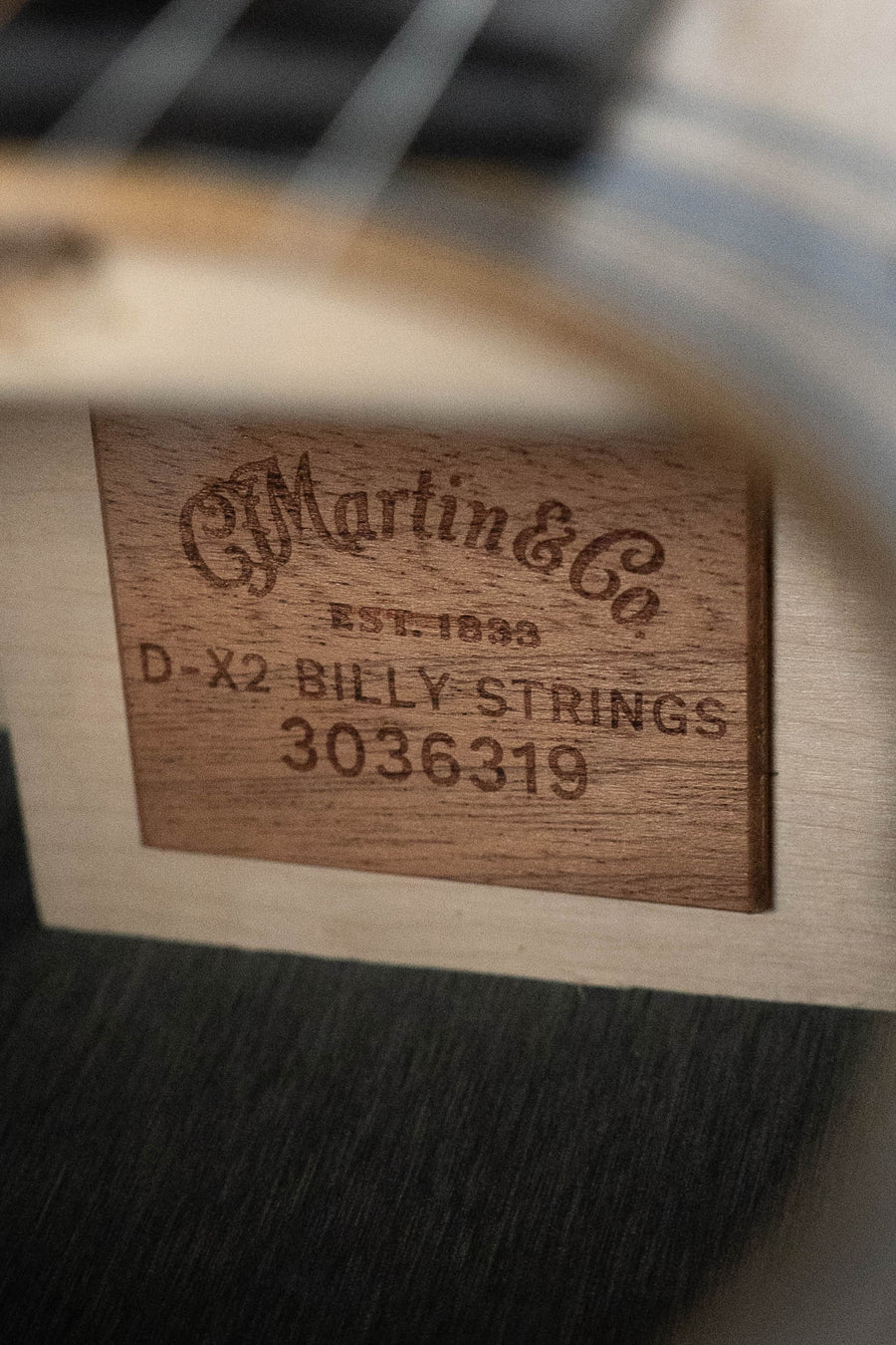 Close-up of a Martin & Co. D-X2E Billy Strings Spruce/HPL Rosewood Dreadnought Guitar label inside the soundhole, reading Martin & Co. EST. 1833 and #6319 on a wooden plaque.