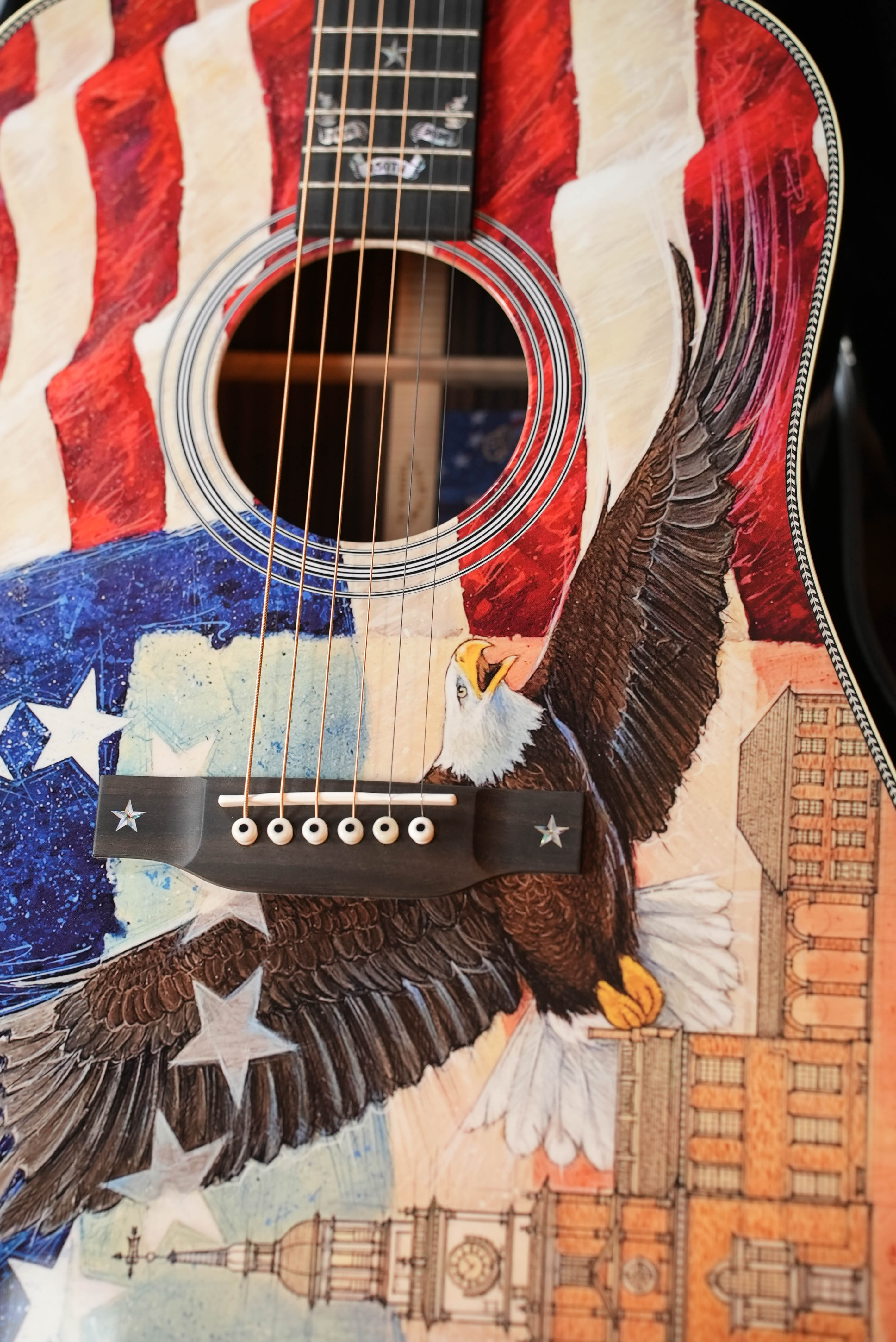 A close-up of the Martin & Co. HD-28 Semiquincentennial Limited Edition Custom Ink Design Acoustic Guitar #7873, featuring patriotic motifs like an American flag, a flying bald eagle, white stars, and buildings on its body.