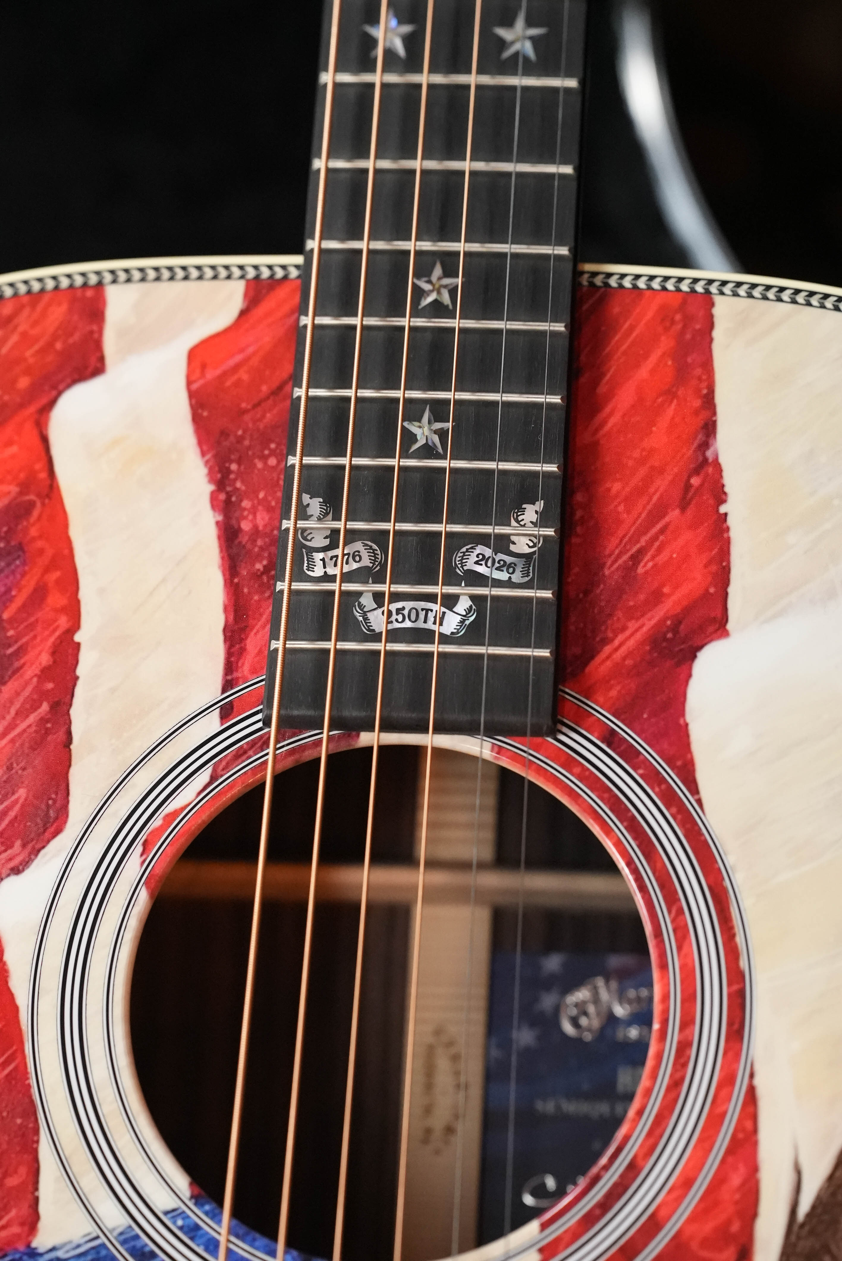 A close-up of the Martin & Co. HD-28 Semiquincentennial Limited Edition Custom Ink Design Acoustic Guitar #7873 shows its American flag motif, star inlays, and banners marking 1776, 2009, and "250th" on the fretboard.