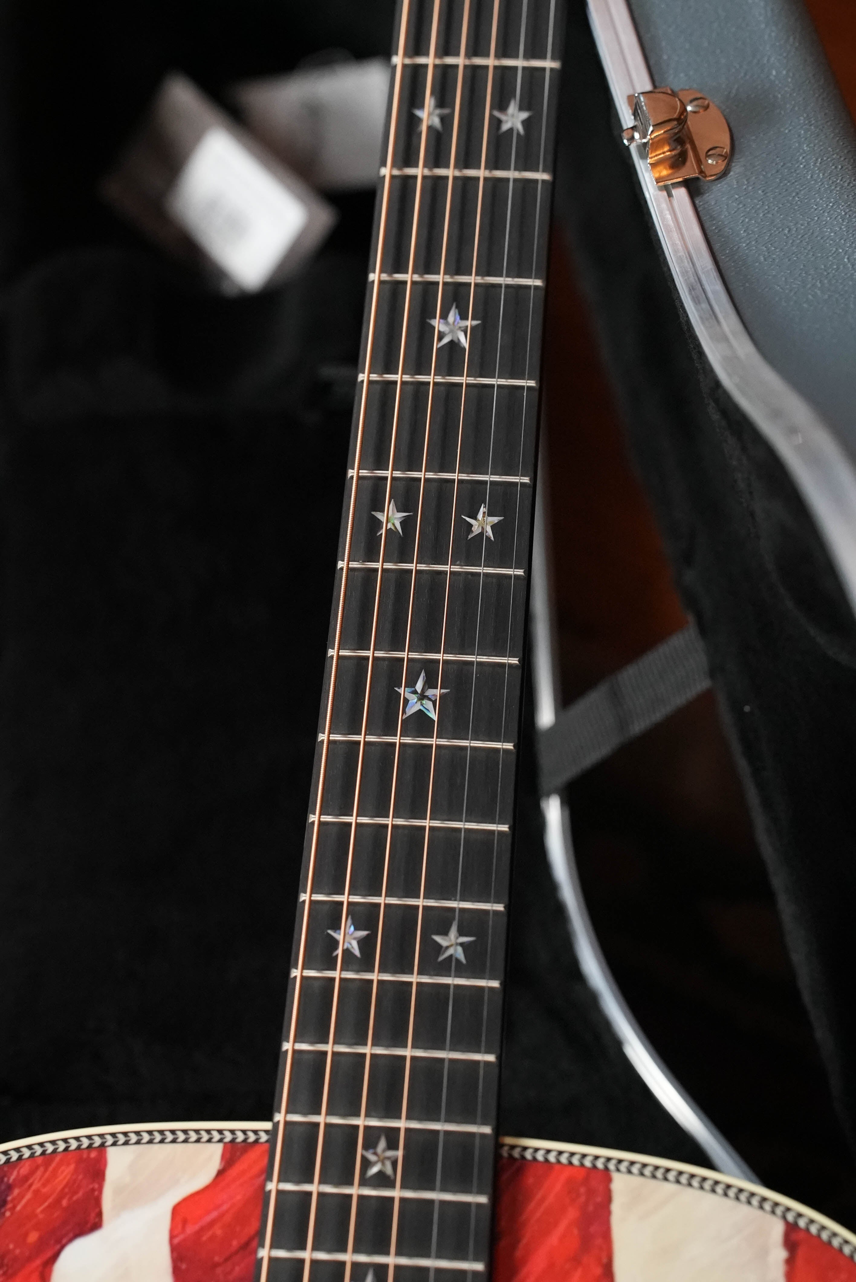 Close-up of the Martin & Co. HD-28 Semiquincentennial Limited Edition Custom Ink Design Acoustic Guitar #7873, showing its neck with star-shaped inlays, bold red and white body, and partially open hard case with visible clasp.